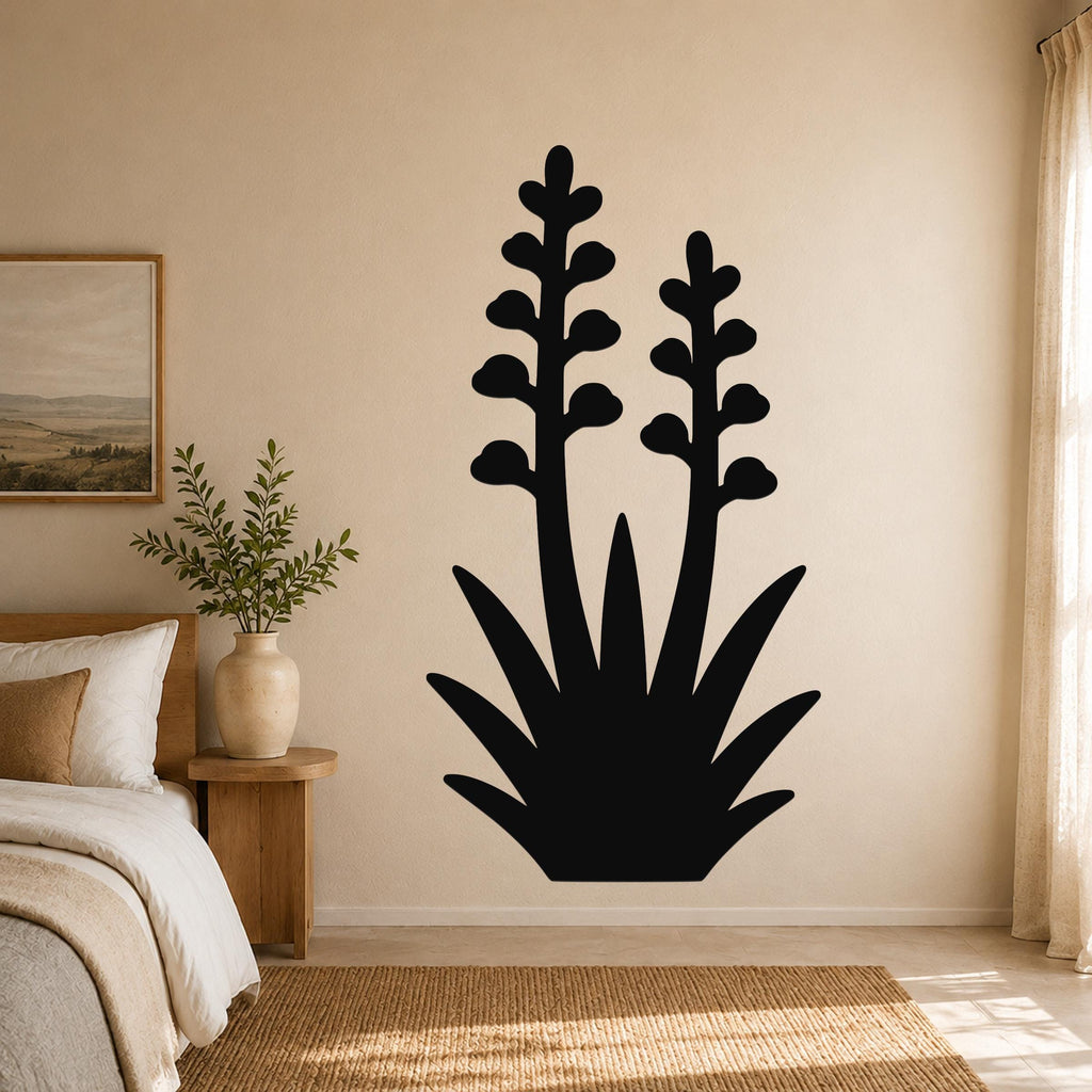 Black metal wall art in the silhouette of a blooming agave plant with two tall flower stalks and spiky leaves, mounted on a beige bedroom wall above a woven rug.