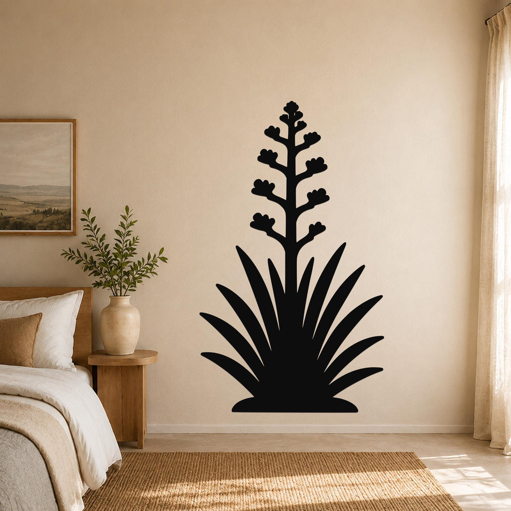 Black metal wall art in the silhouette of a blooming agave plant, mounted on a beige bedroom wall above a woven rug.