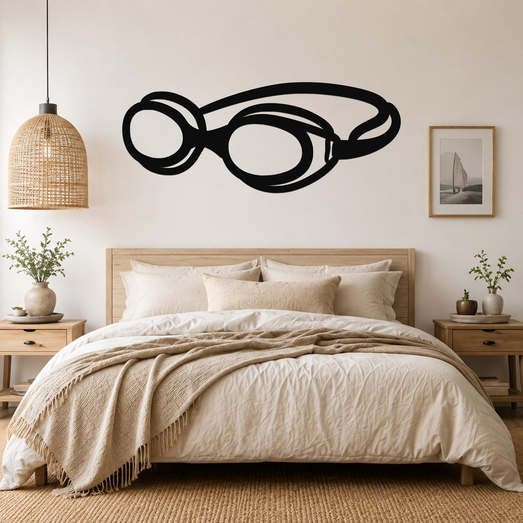 Black metal swim goggles wall art silhouette mounted above a bed in a neutral bedroom.