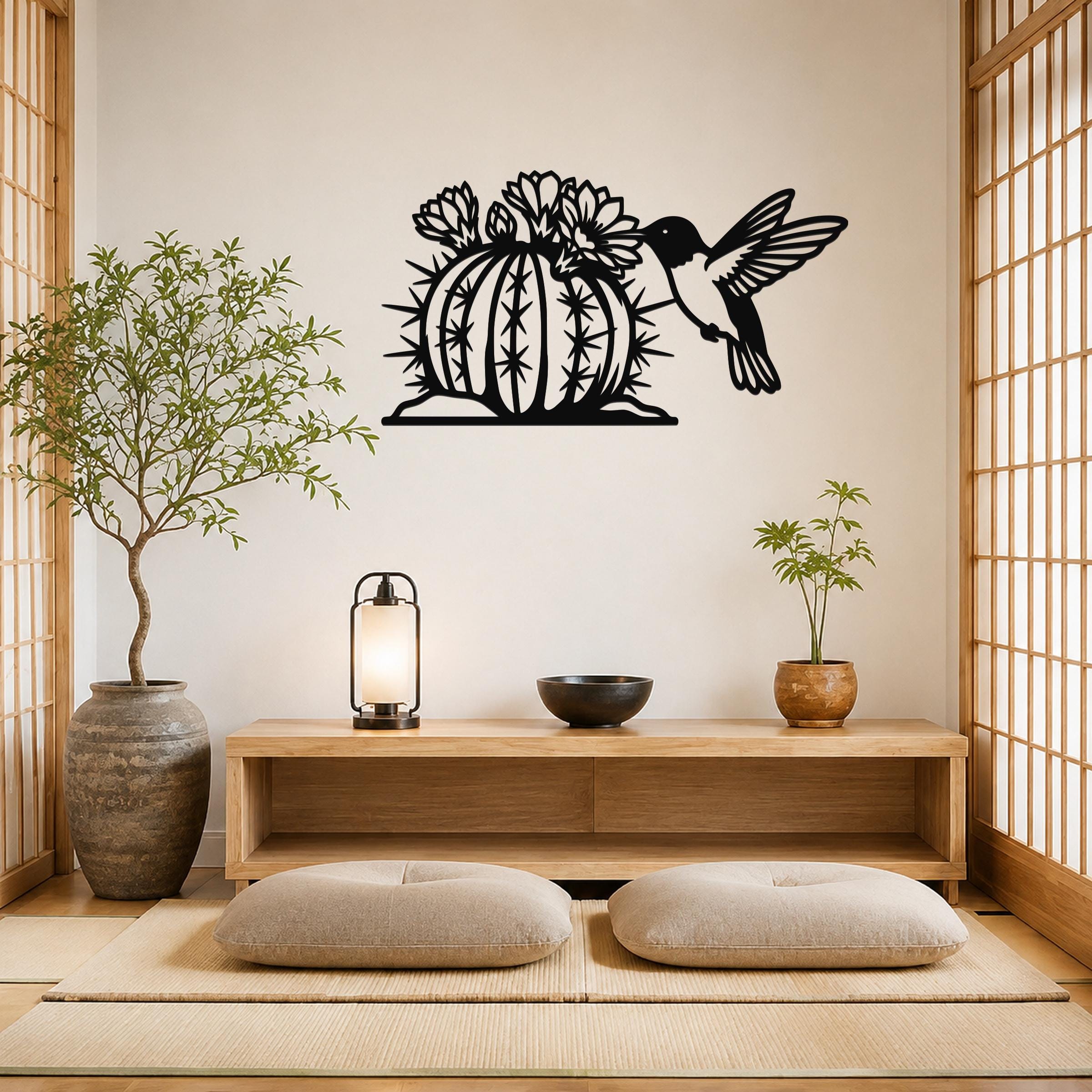 Black metal wall art featuring a hummingbird and flowering barrel cactus cutout, mounted on a light-colored wall above a wooden console in a minimalist room.
