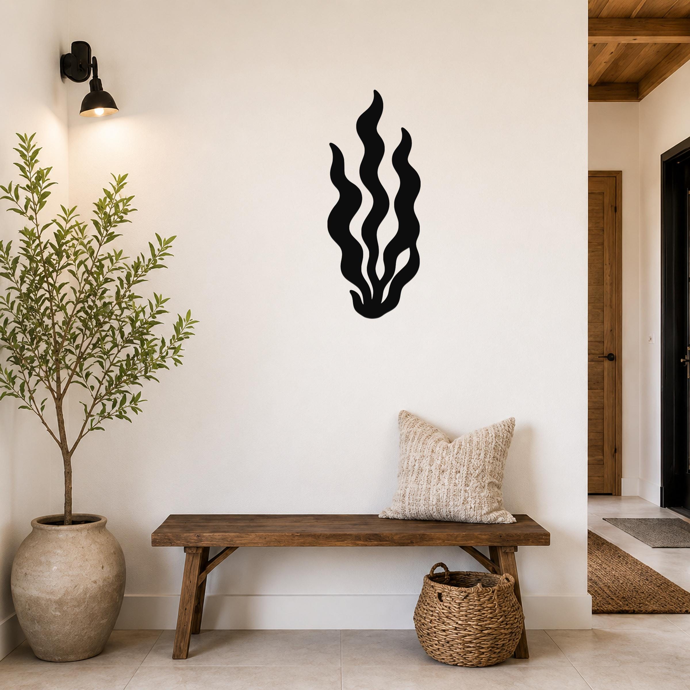 Black metal kelp wall art with flowing wavy cutouts, mounted on a white wall above a wooden bench in a modern entryway.