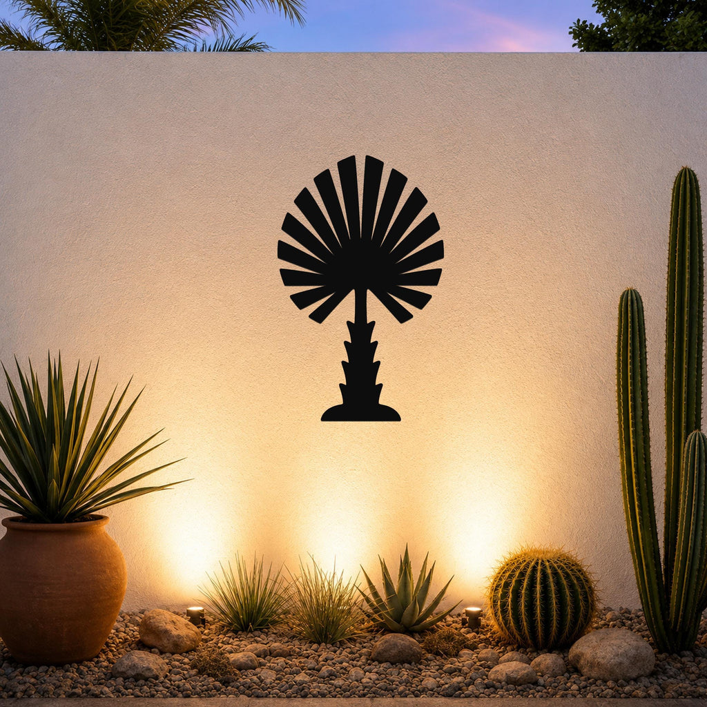 Black metal palm tree wall art with fan-shaped fronds, mounted on a textured outdoor wall above a desert garden with cacti and warm uplighting.