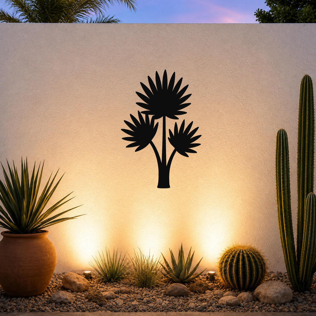 Black metal wall art silhouette of a fan palm tree with three fronds, mounted on an outdoor wall above a desert garden with cacti and warm uplighting.