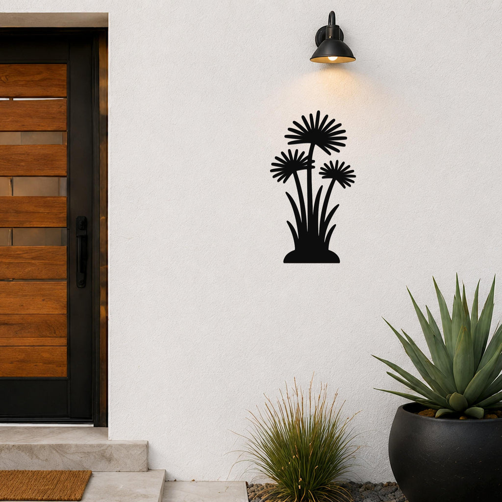 Black metal wall art featuring a silhouette of three wildflowers with spiky petals and long stems, mounted on an outdoor wall beside a front door and potted plants.