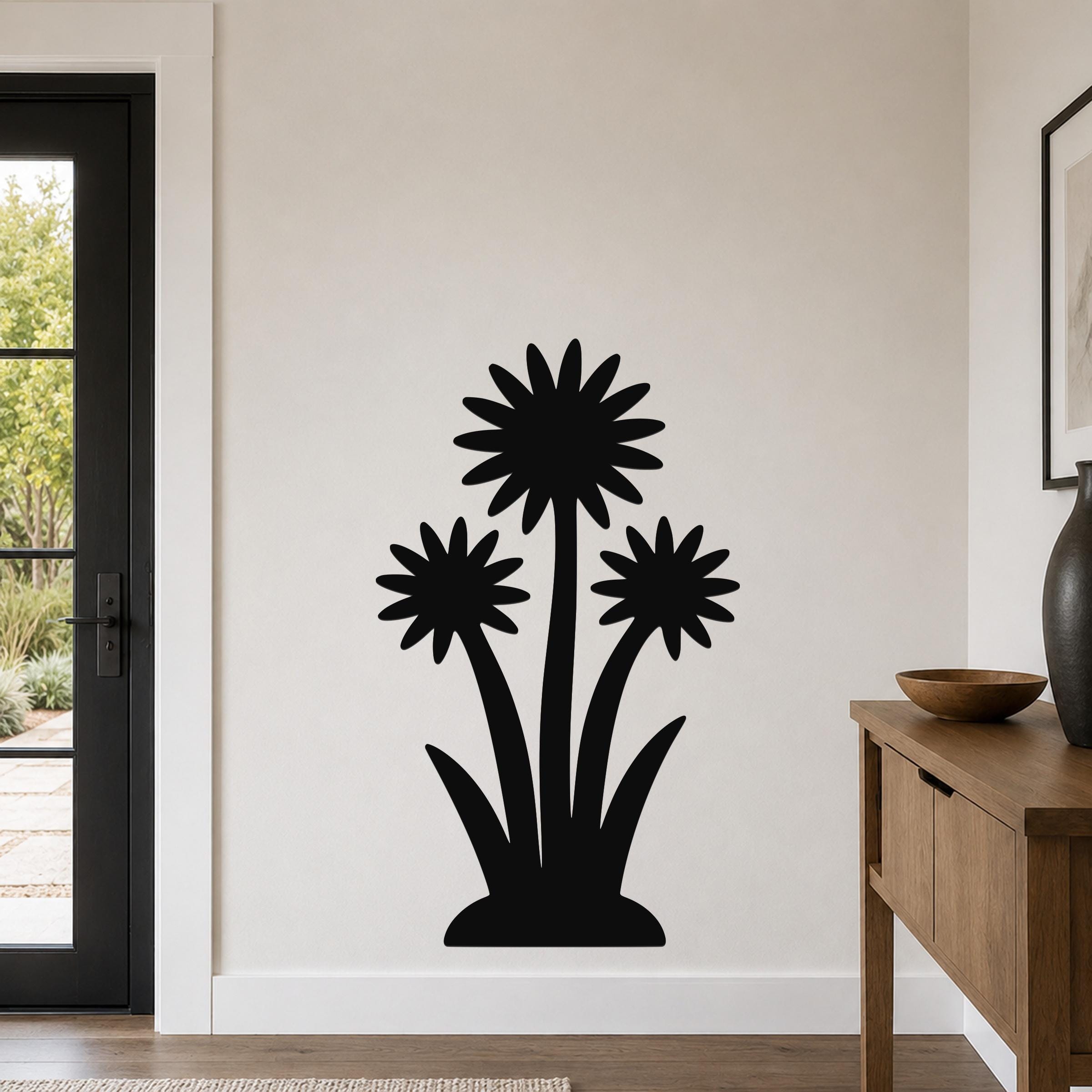 Black metal wall art featuring a silhouette of three wildflowers with long stems and pointed leaves, mounted on a light-colored wall in a living room.