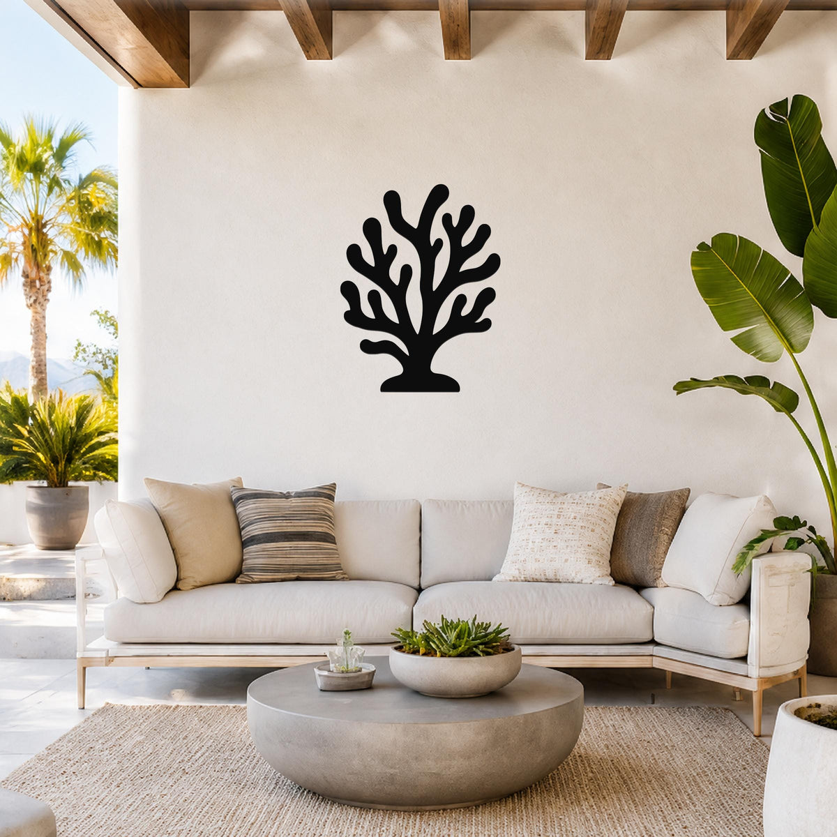 Black metal coral wall art with branching cutouts, mounted on a white wall above a light-colored sofa in a bright living room.