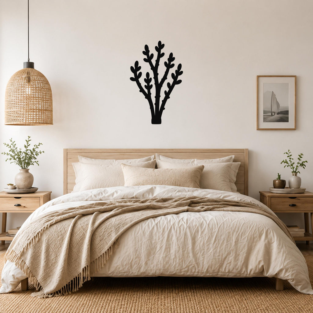 Black metal wall art in a desert branch silhouette, mounted above a bed in a neutral bedroom.