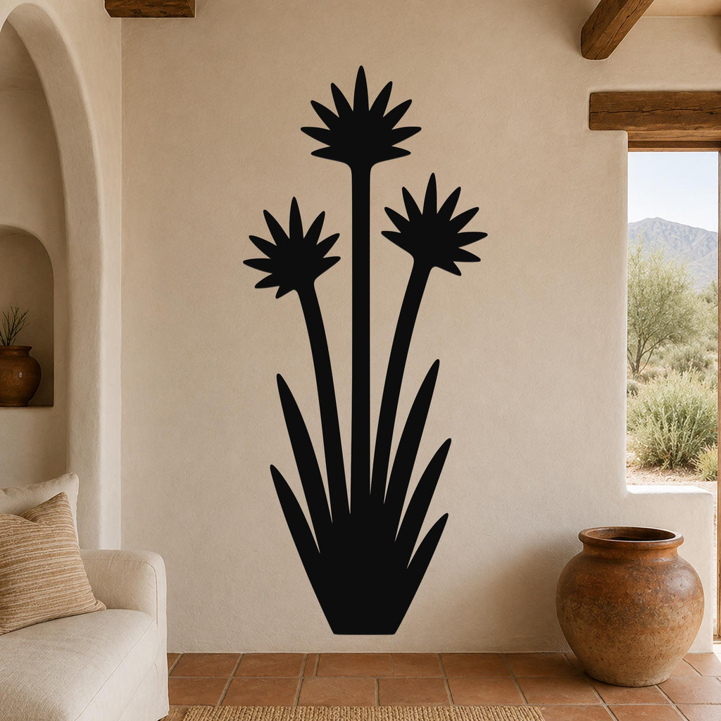 Black metal yucca wall art with three blooming flower silhouettes and long leaves, mounted on a beige living room wall above a sofa.