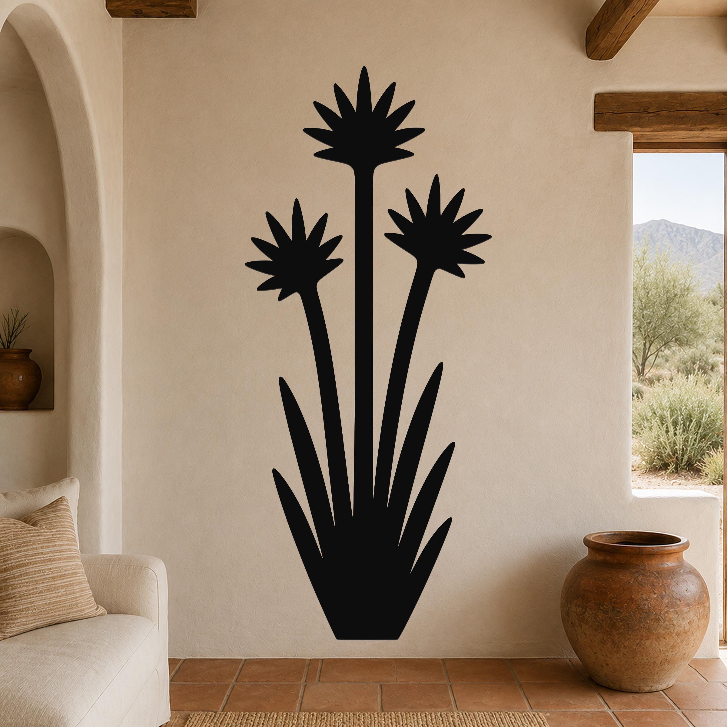 Black metal yucca wall art with three blooming flower silhouettes and long leaves, mounted on a beige living room wall above a sofa.