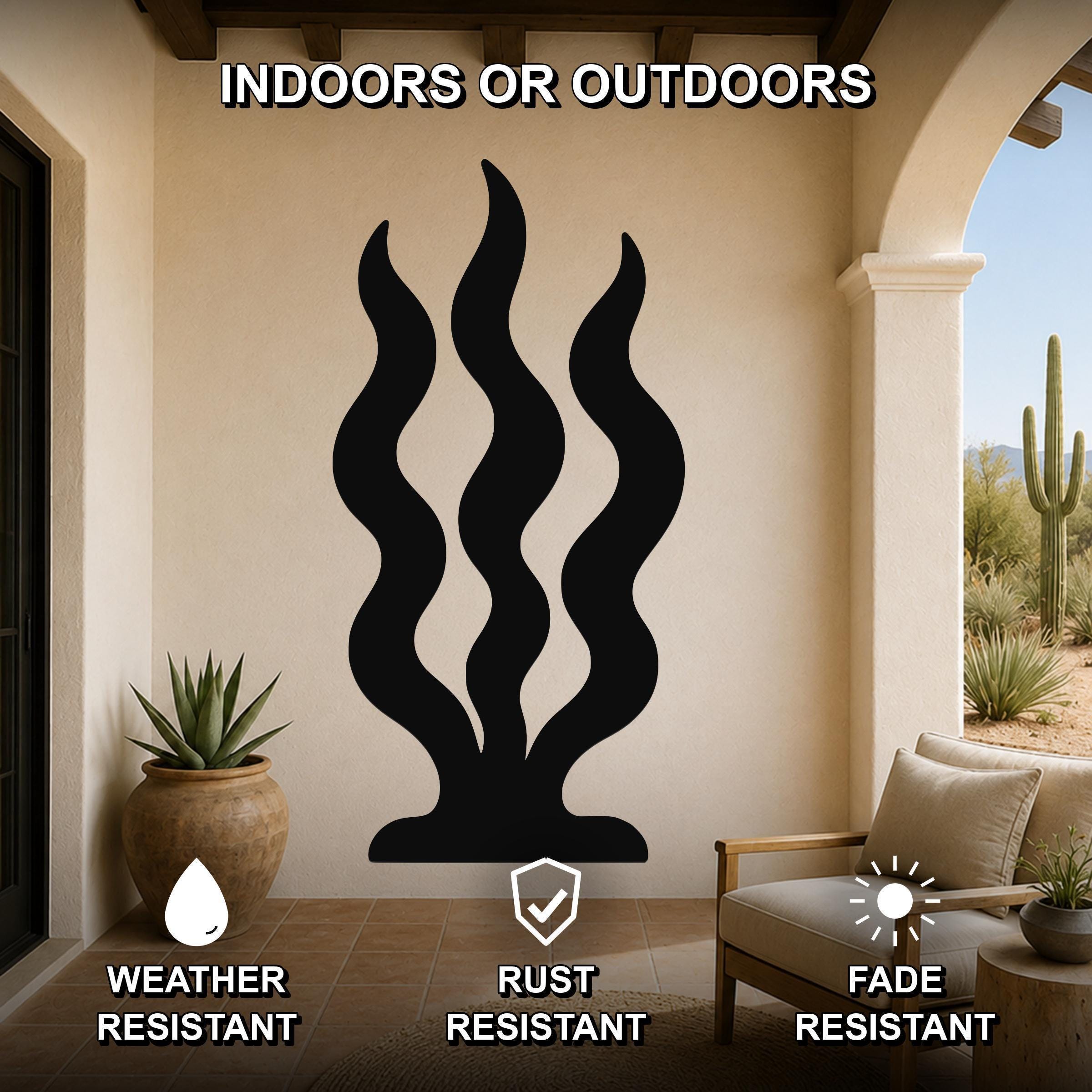 Black metal wall art with wavy grass cutouts, mounted on a beige outdoor patio wall above a chair and potted plant.