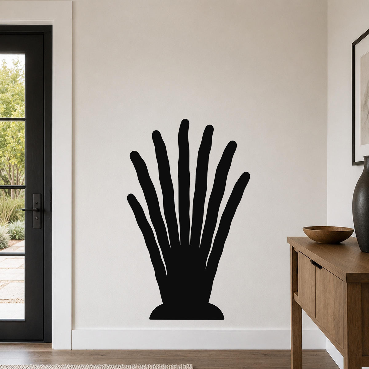 Black metal wall art in a silhouette of a hand with spread fingers, mounted on a light-colored wall in a modern entryway.