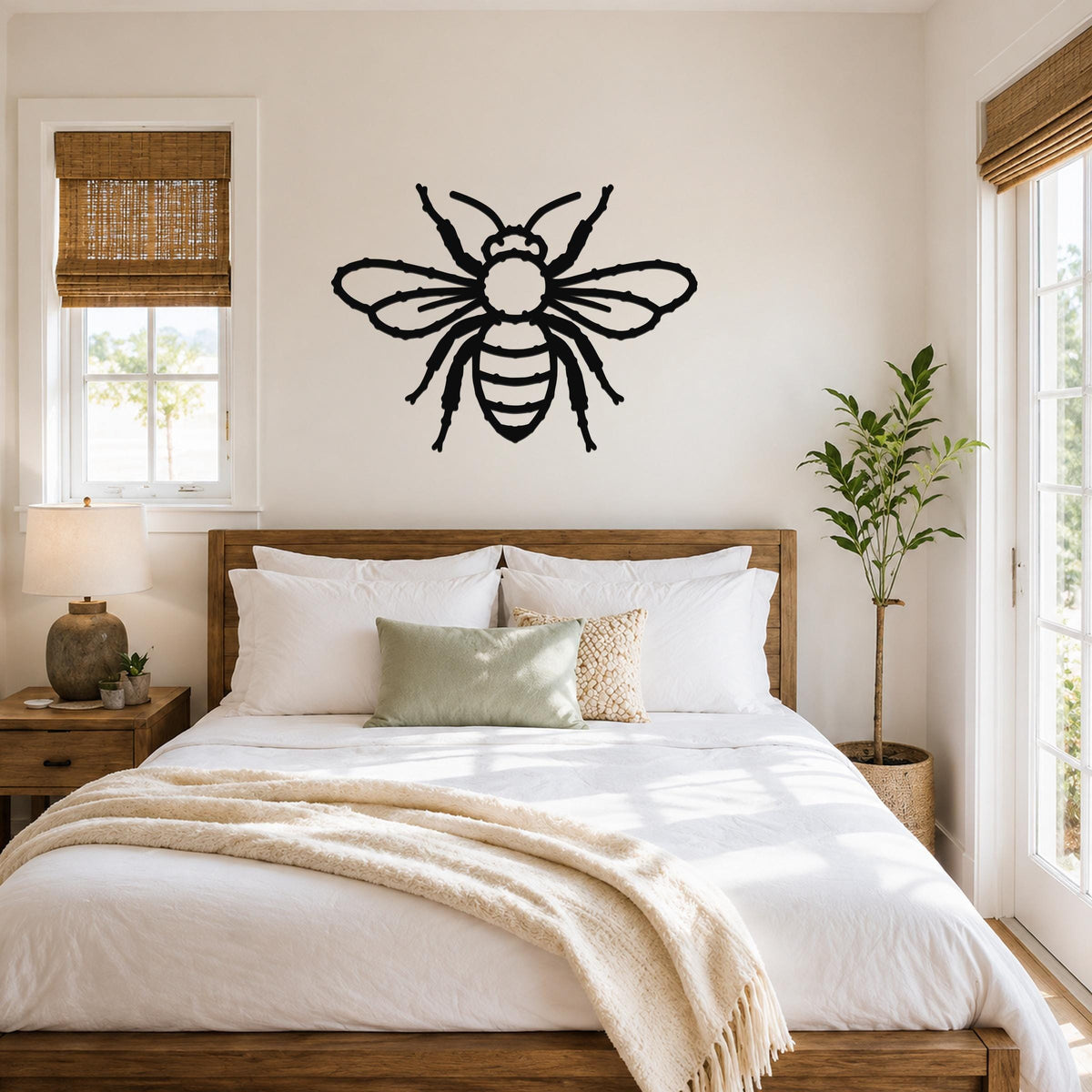 Black metal bee wall art with cutout wings and body, mounted above a wooden bed in a bright bedroom.