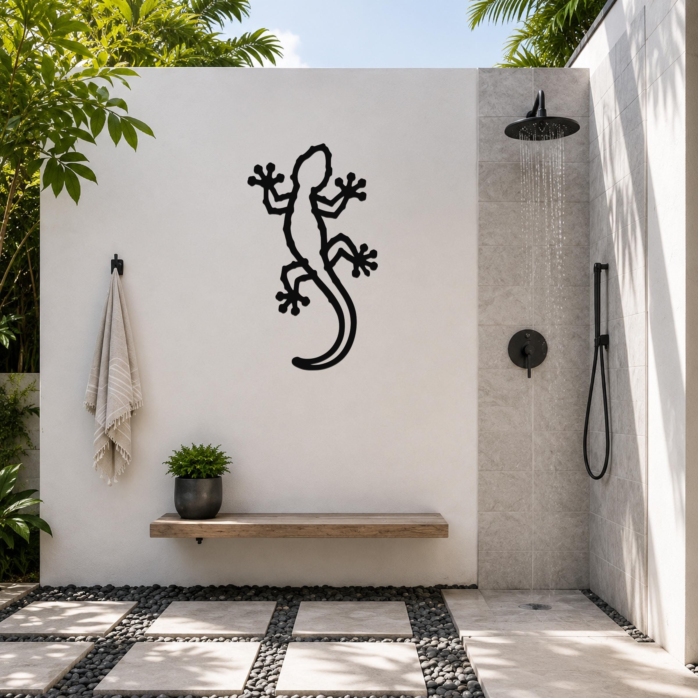 Black metal lizard wall art with cutout details, mounted on a white outdoor wall above a wooden bench in a patio shower area.