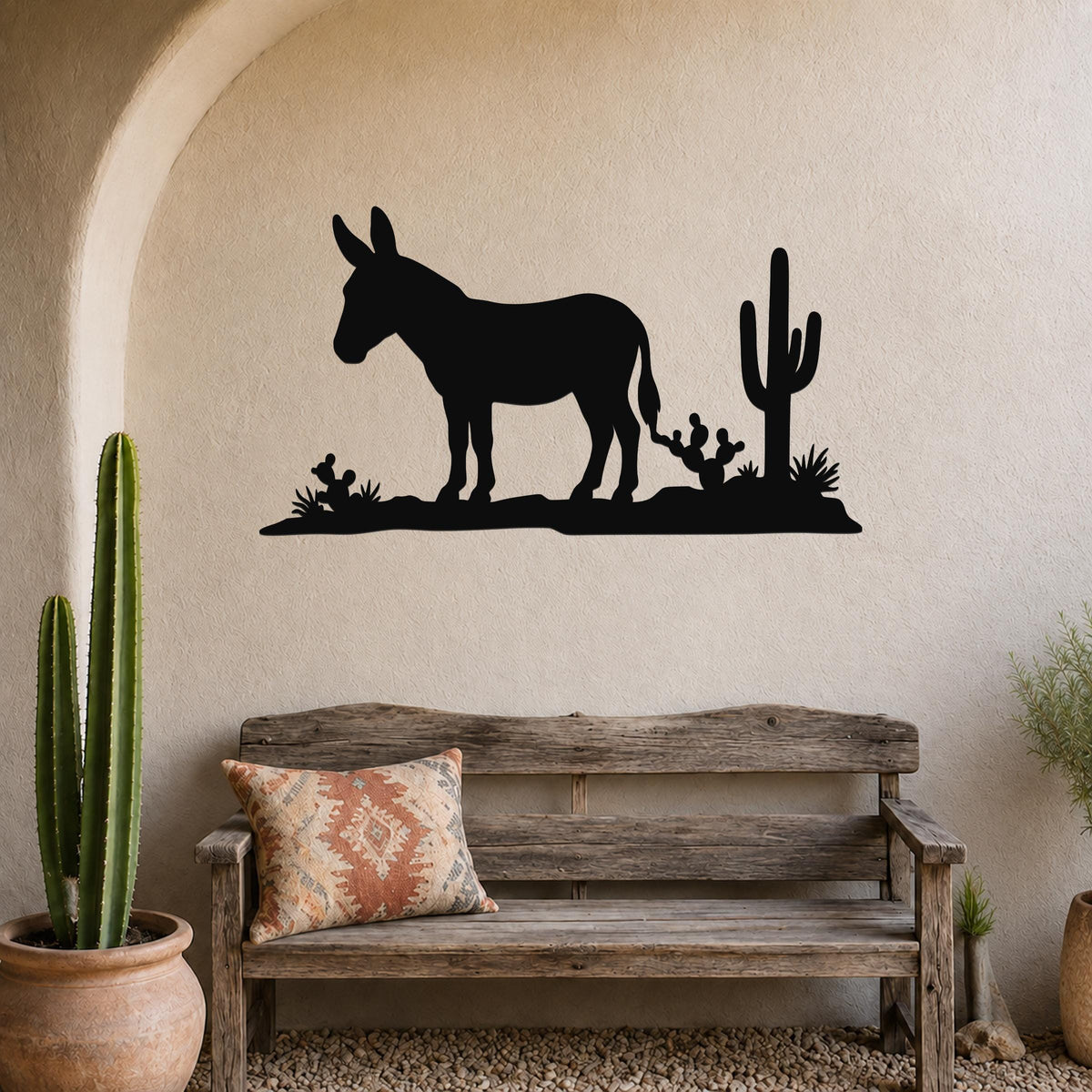 Black metal wall art silhouette of a burro and cacti, mounted above a wooden bench in a rustic indoor space.