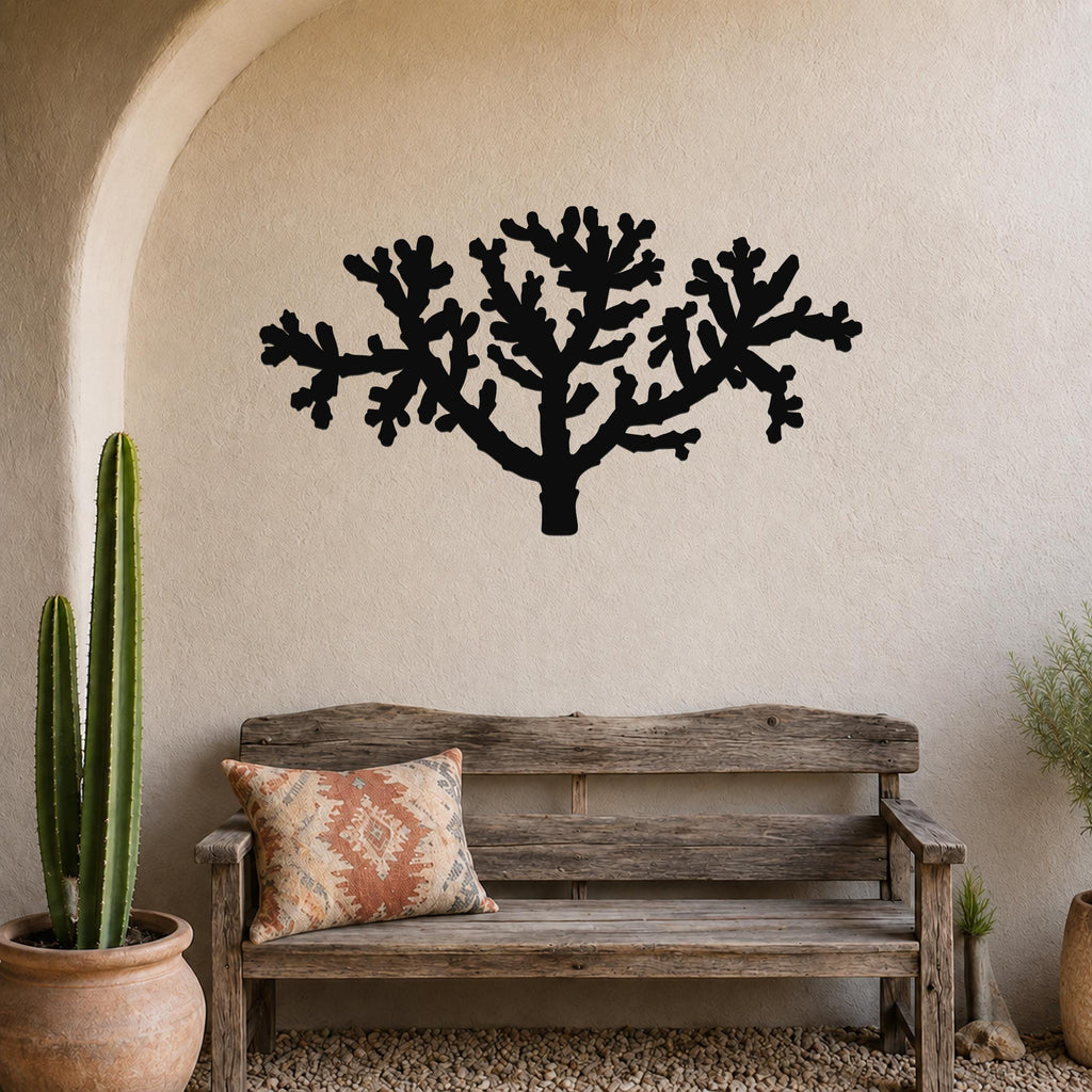 Black metal Cholla cactus wall art silhouette with branching cutouts, mounted on a textured beige wall above a rustic wooden bench in a southwestern-style entryway.