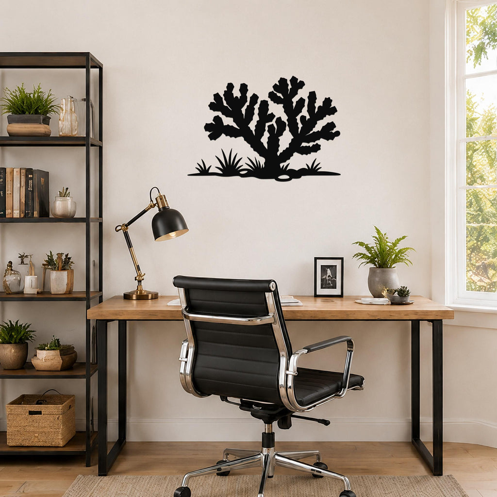 Black metal Cholla cactus wall art with branching silhouette and ground-level spiky plants, mounted on a light-colored wall above a wooden desk in a home office.