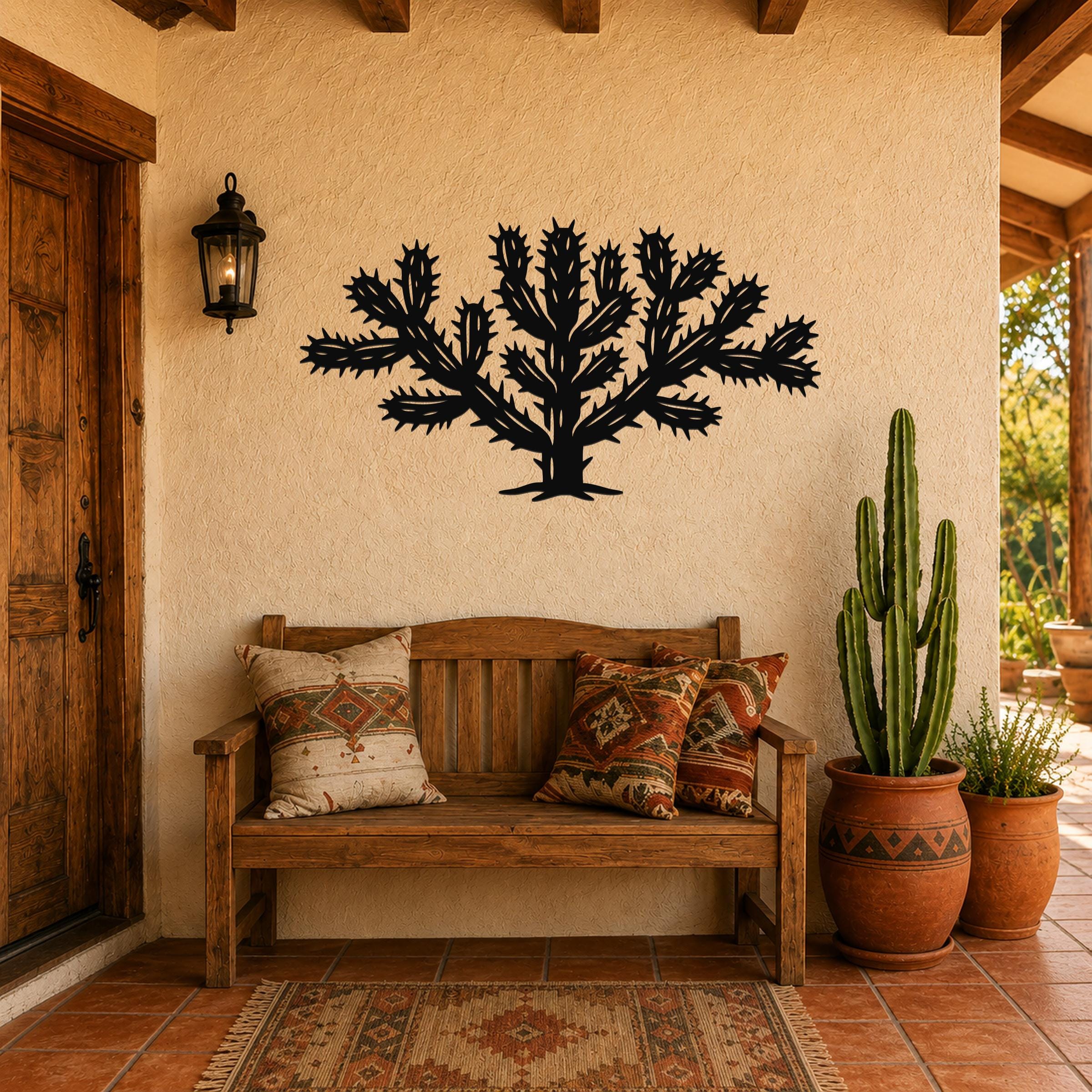 Black metal cholla cactus wall art with spiky branch cutouts, mounted on a stucco wall above a wooden bench on a patio.