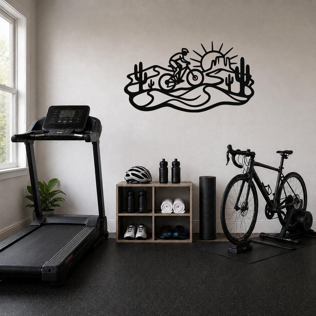 Black metal wall art with a desert silhouette of a cyclist, cacti, and sun, mounted on a wall above a shelving unit in a home gym.