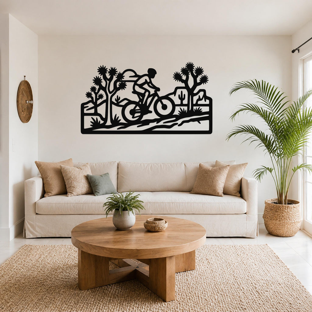 Black metal wall art cutout of a cyclist riding through a Joshua tree desert scene, mounted above a sofa in a living room.