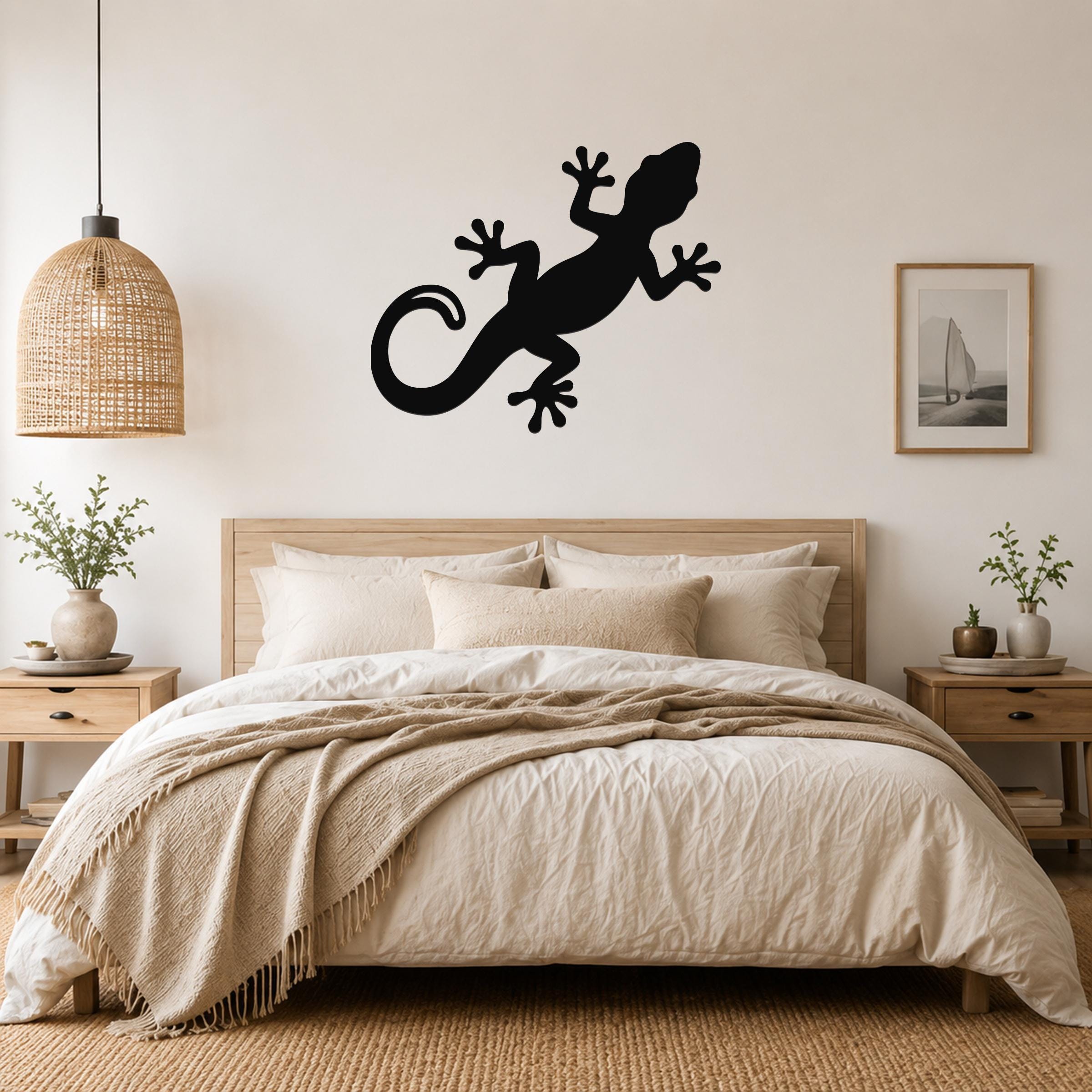 Black metal gecko wall art silhouette mounted above a bed in a neutral bedroom.