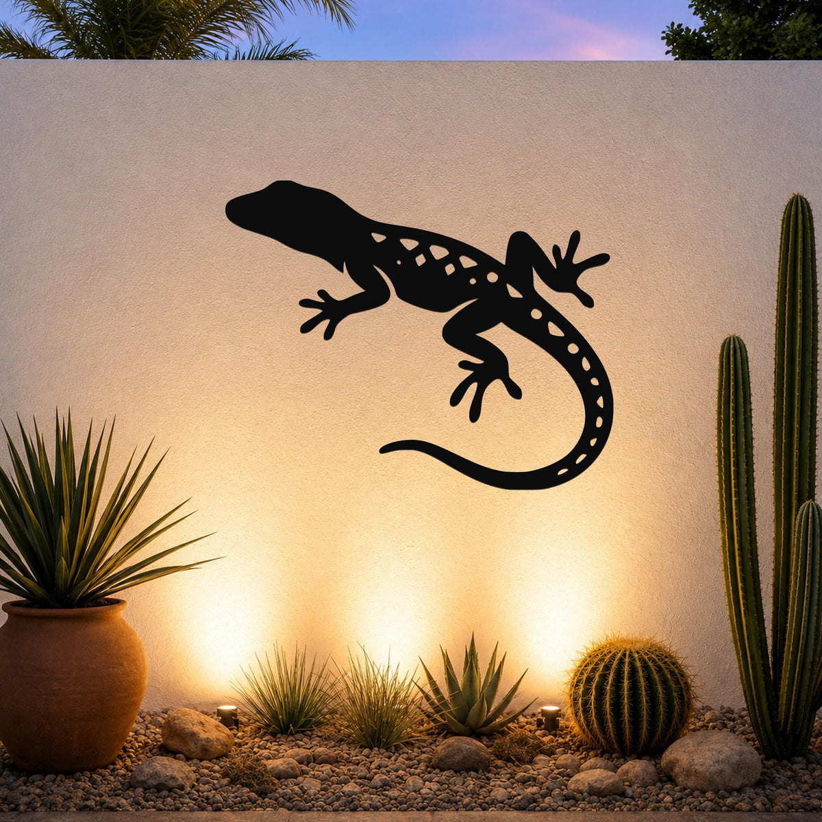 Black metal lizard wall art with internal cutout details, mounted on a textured outdoor wall above a desert garden with cacti and warm uplighting.