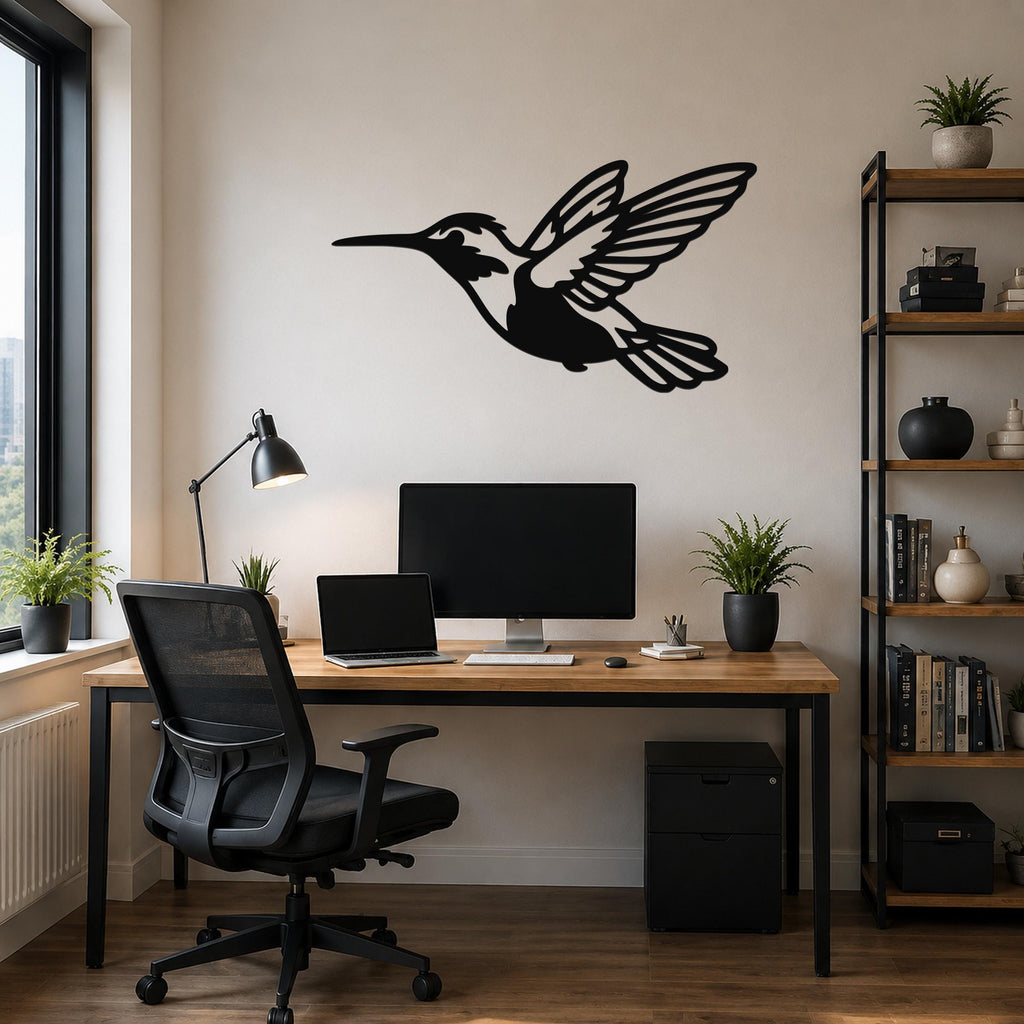 Black metal hummingbird wall art with open wings and internal cutout details, mounted on a wall above a wooden desk in a home office.
