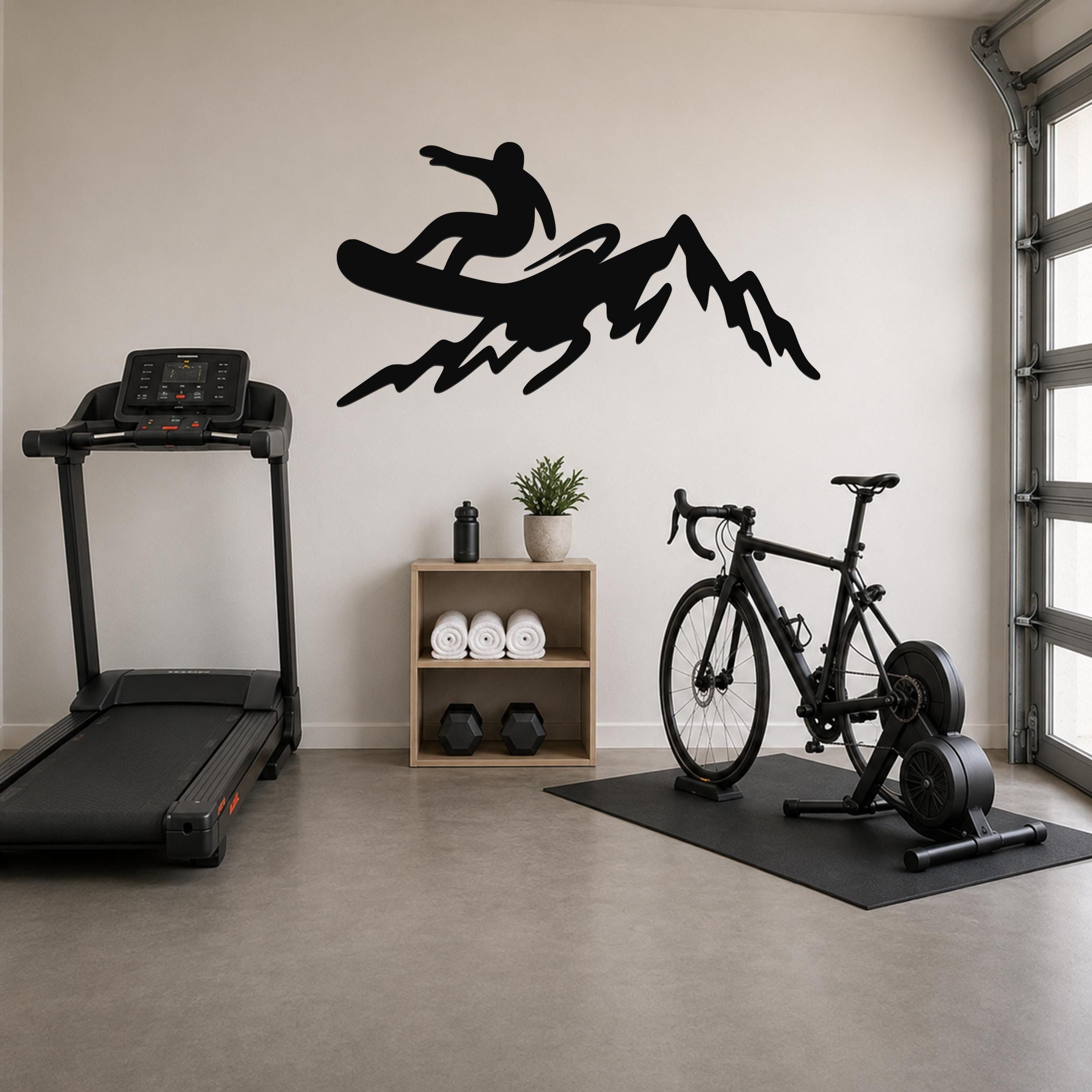 Black metal wall art silhouette of a snowboarder on a mountain, mounted on a wall above a wooden shelf in a home gym.