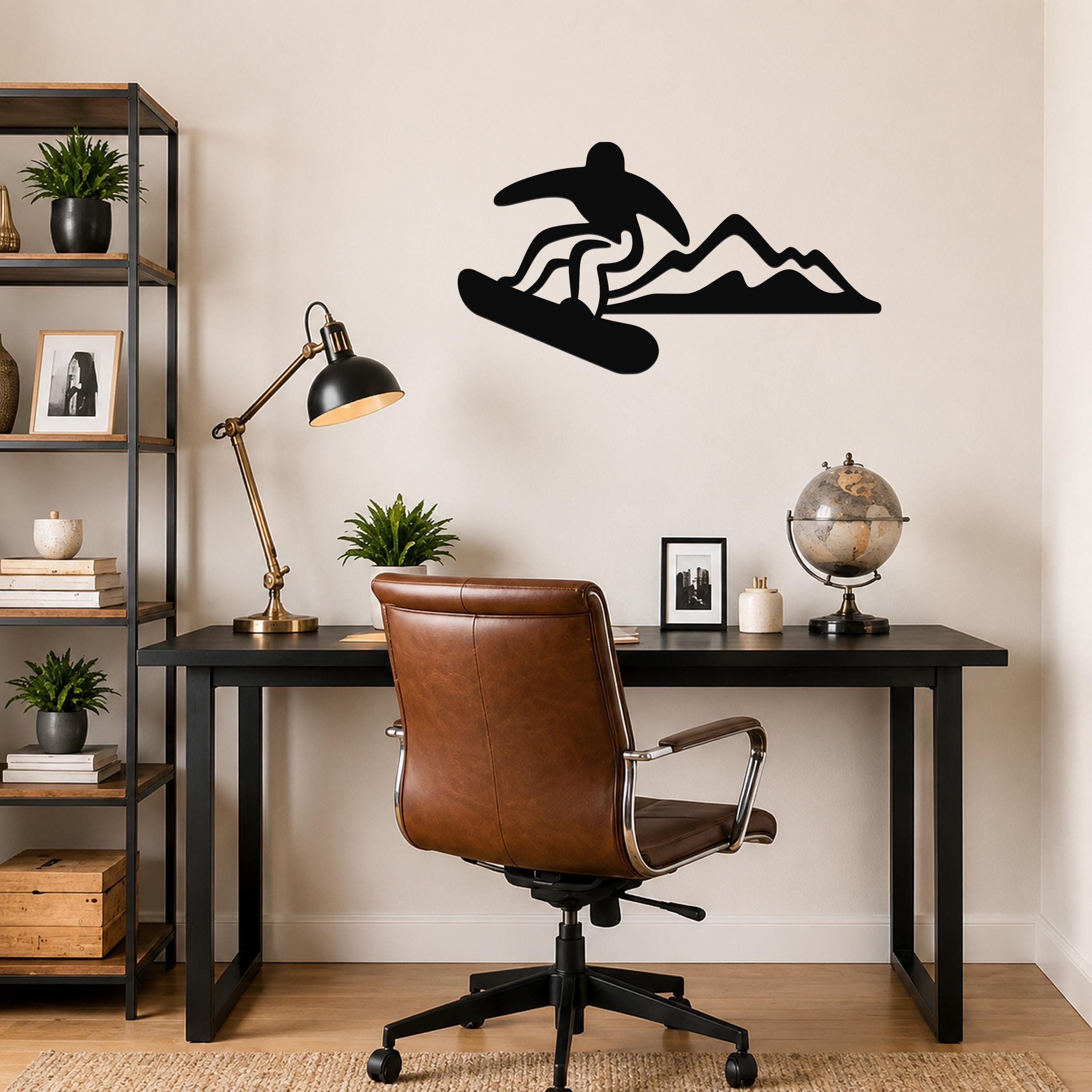 Black metal wall art silhouette of a snowboarder in motion above a desk, mounted on a light-colored wall in a home office.