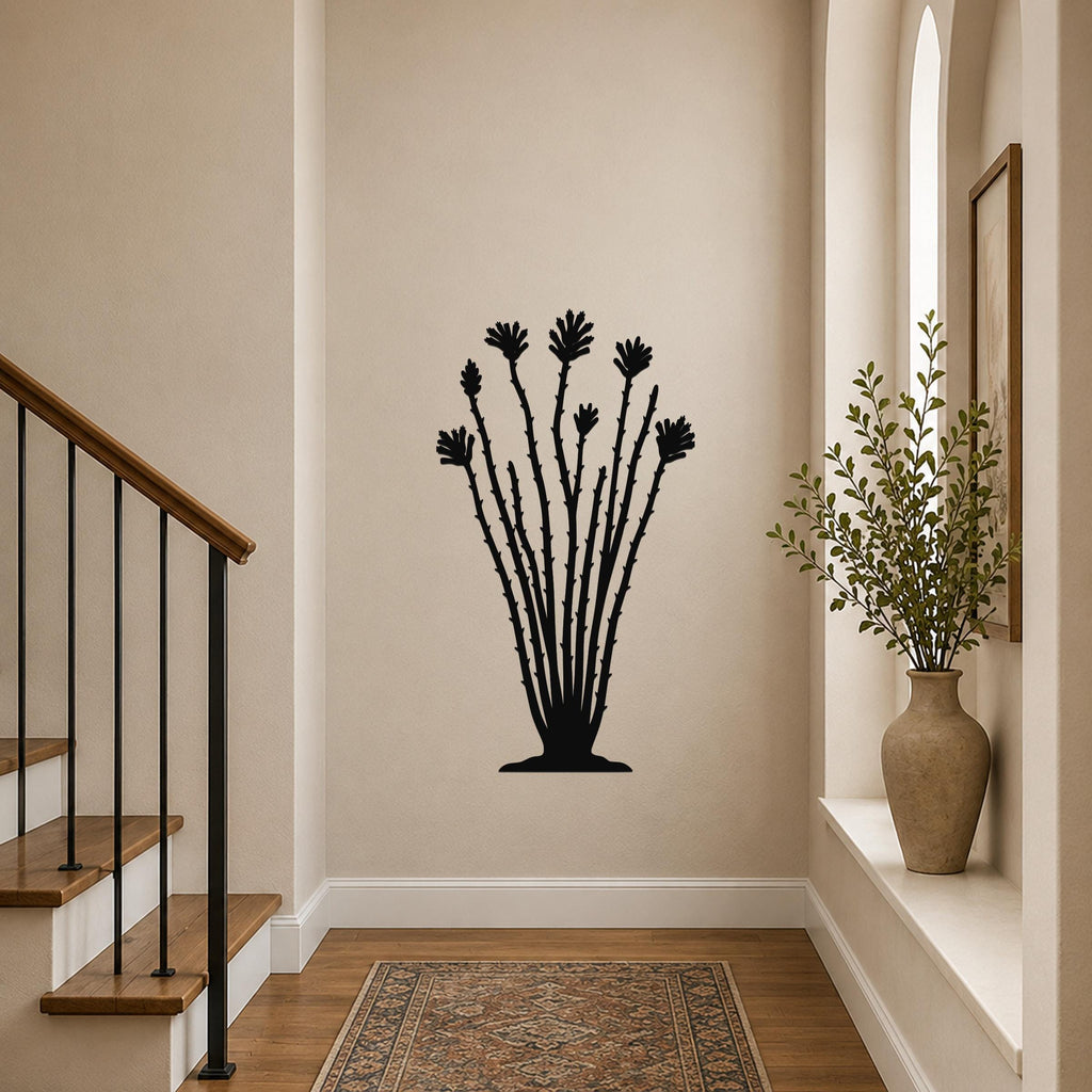 Black metal ocotillo wall sculpture with spiny branches and flower cutouts, mounted on a beige hallway wall above a patterned rug.