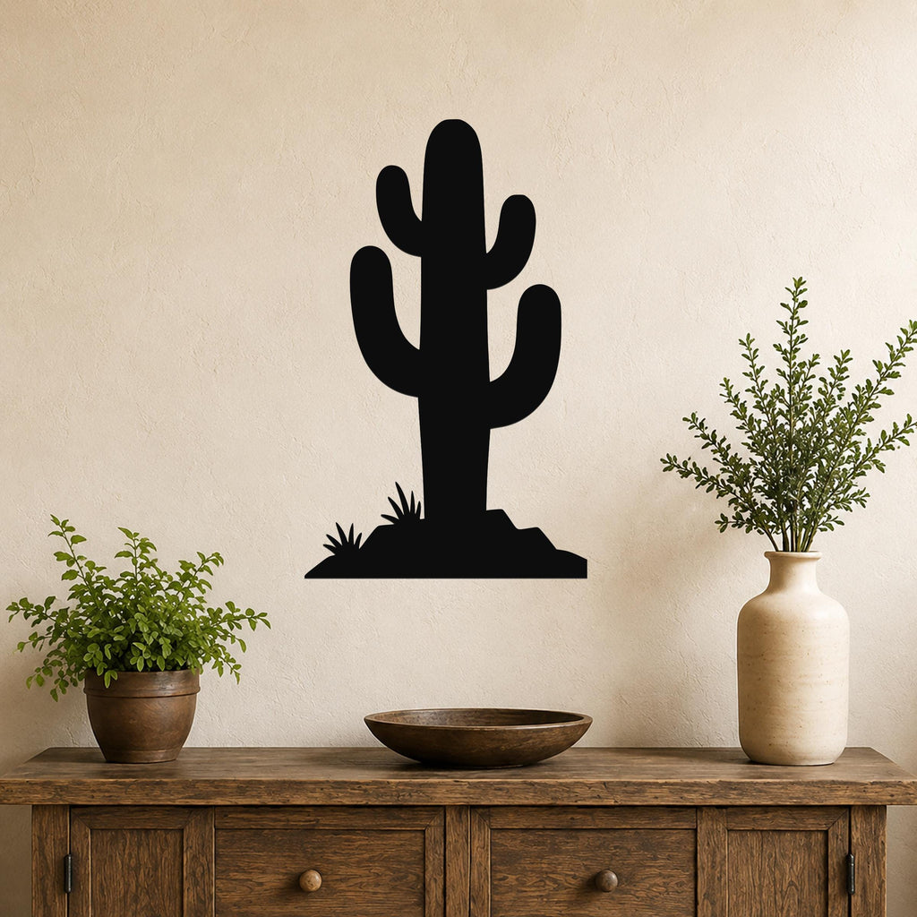 Black metal cactus wall art with a silhouette of a saguaro and small desert plants, mounted on a beige wall above a wooden console table.