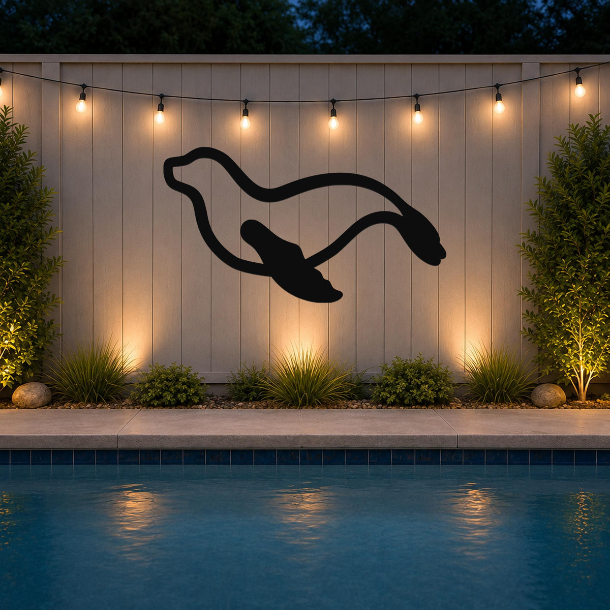 Black metal sea lion wall art with motion-line cutouts, mounted on a light-colored outdoor wall above a pool at night.