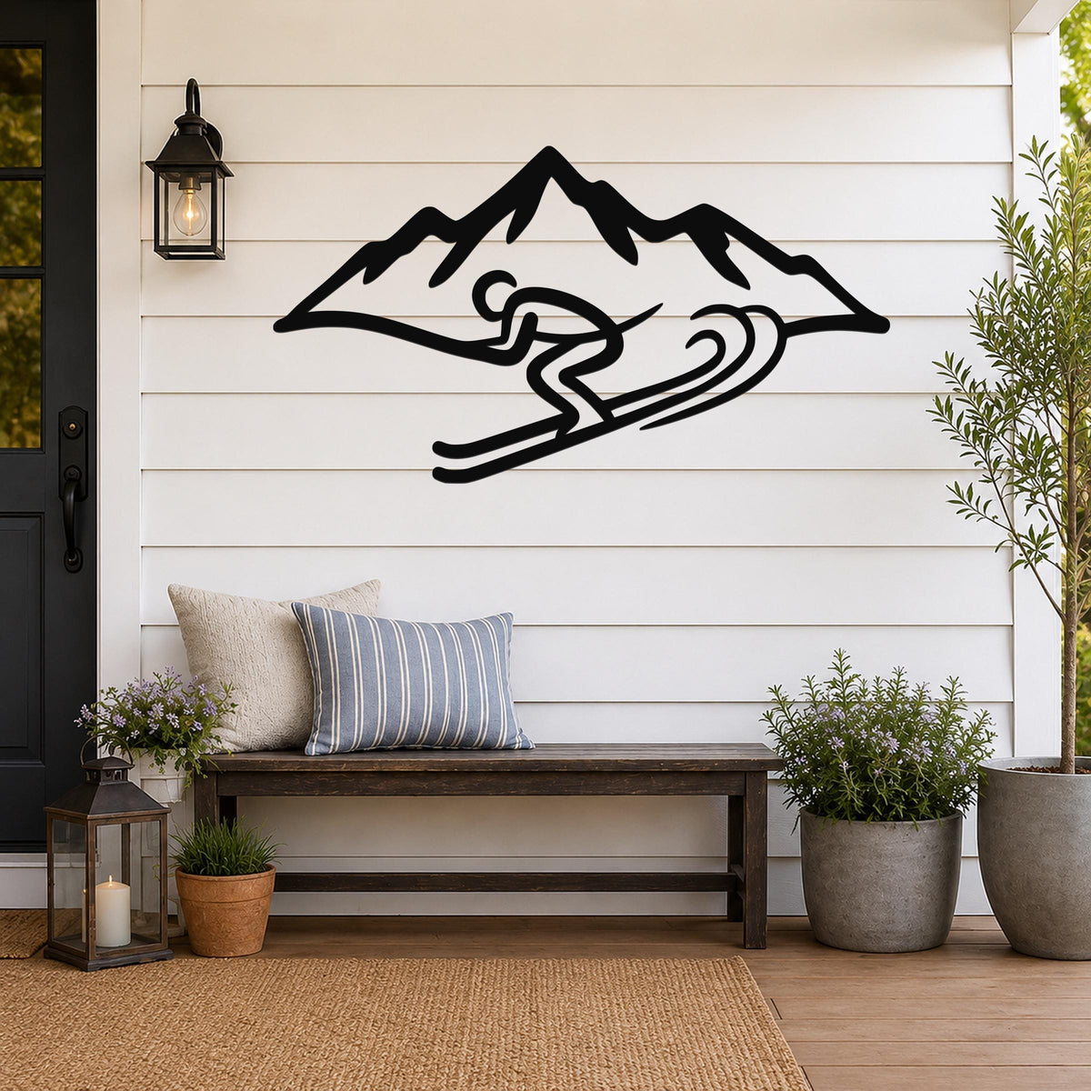 Black metal wall art featuring a skier silhouette in motion with mountain peaks, mounted on a white shiplap wall above a wooden bench on a porch.