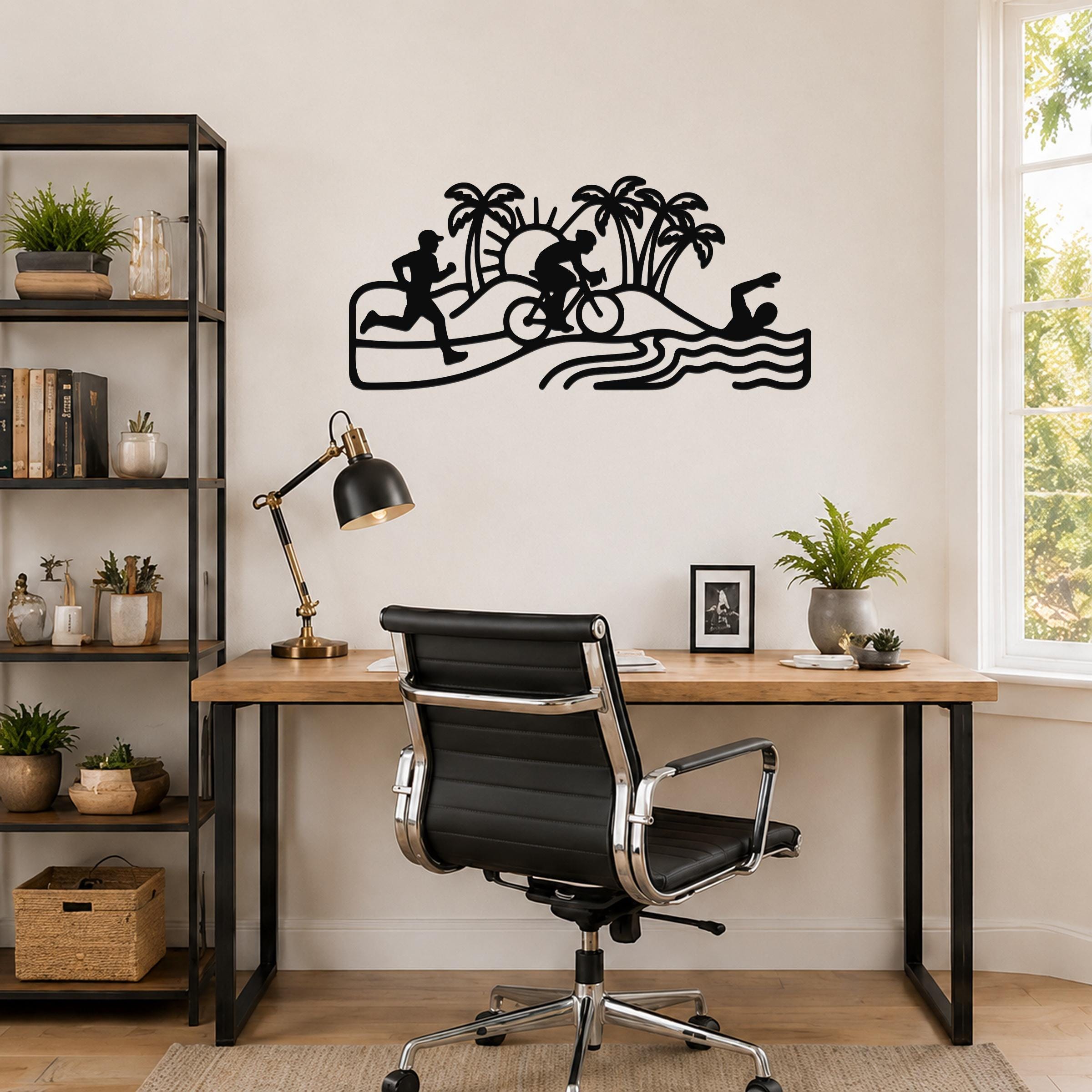 Black metal triathlon wall art with swim, bike, and run silhouettes, palm trees, and waves, mounted above a wooden desk in a home office.