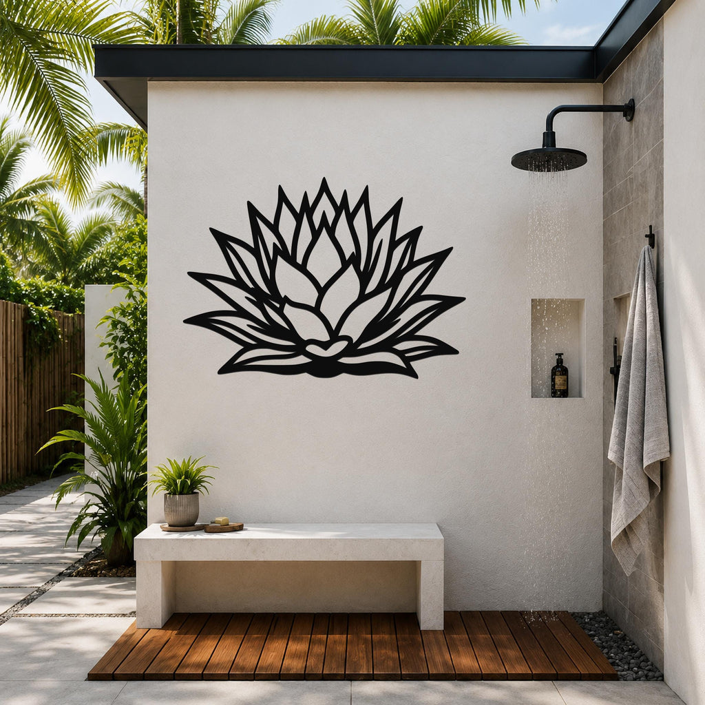 Black metal agave wall sculpture with layered leaf cutouts, mounted on a white outdoor shower wall above a stone bench.