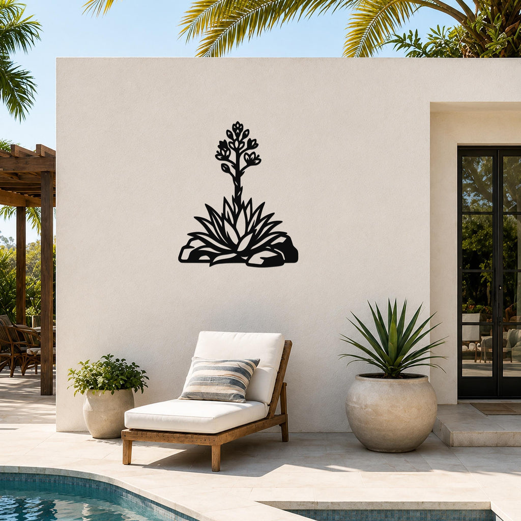 Black metal agave wall art with blooming flower cutout, mounted on a white outdoor wall beside a pool and lounge chair.