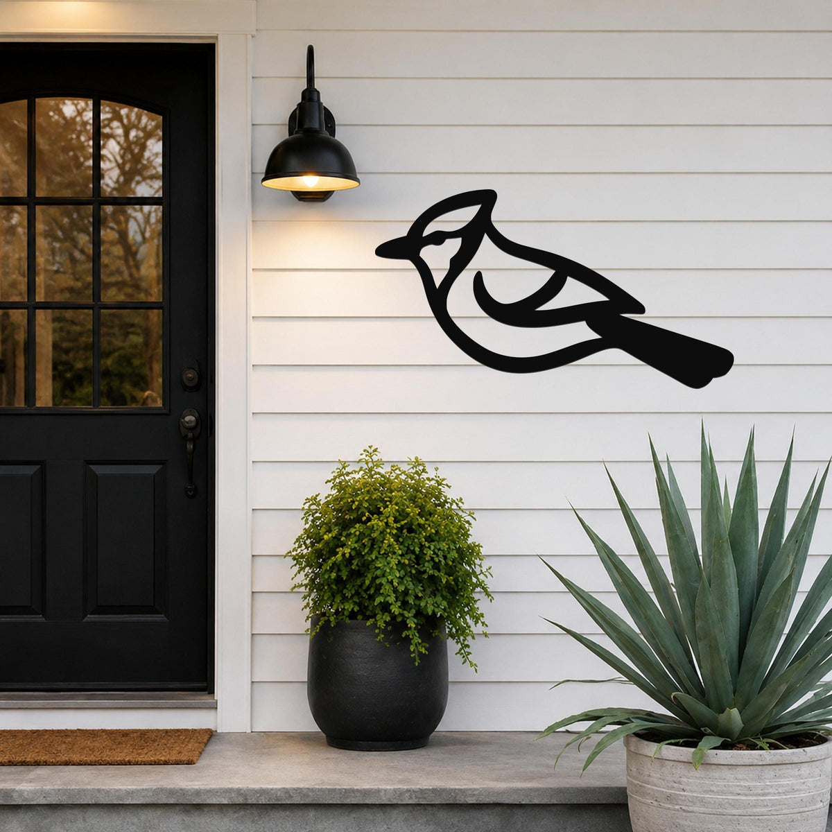 Black metal blue jay wall art silhouette mounted on a white siding wall beside a black front door and outdoor light.