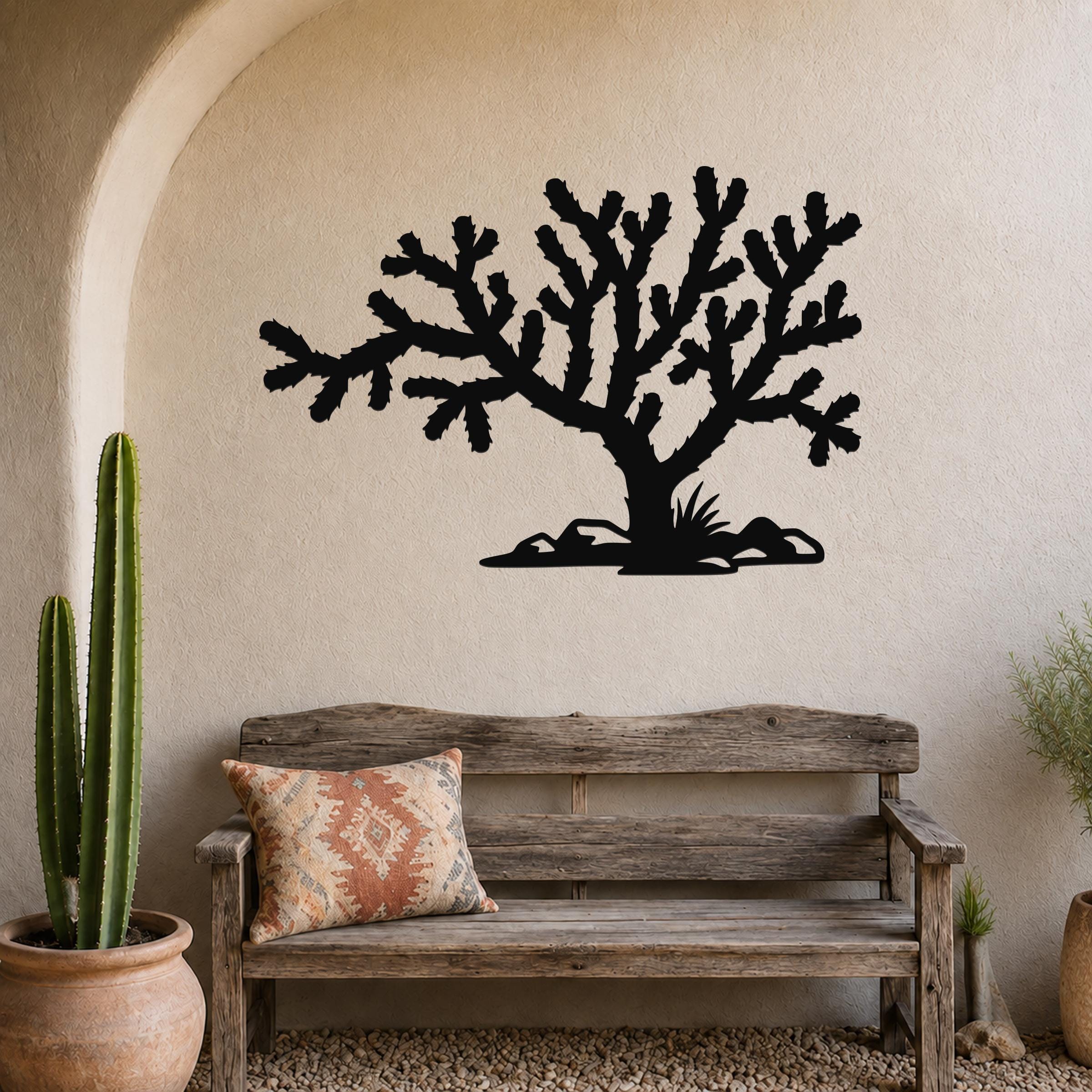 Black metal Cholla cactus wall art silhouette with branching arms and base cutouts, mounted on a textured beige wall above a rustic wooden bench in a desert-themed entryway.