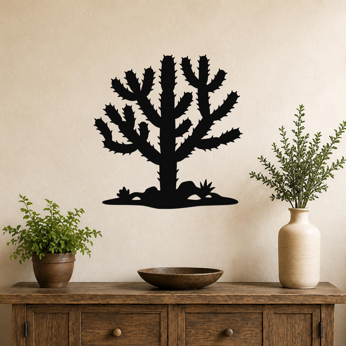 Black metal Cholla cactus wall art silhouette with spiny branches and ground cutouts, mounted on a beige wall above a wooden console table.