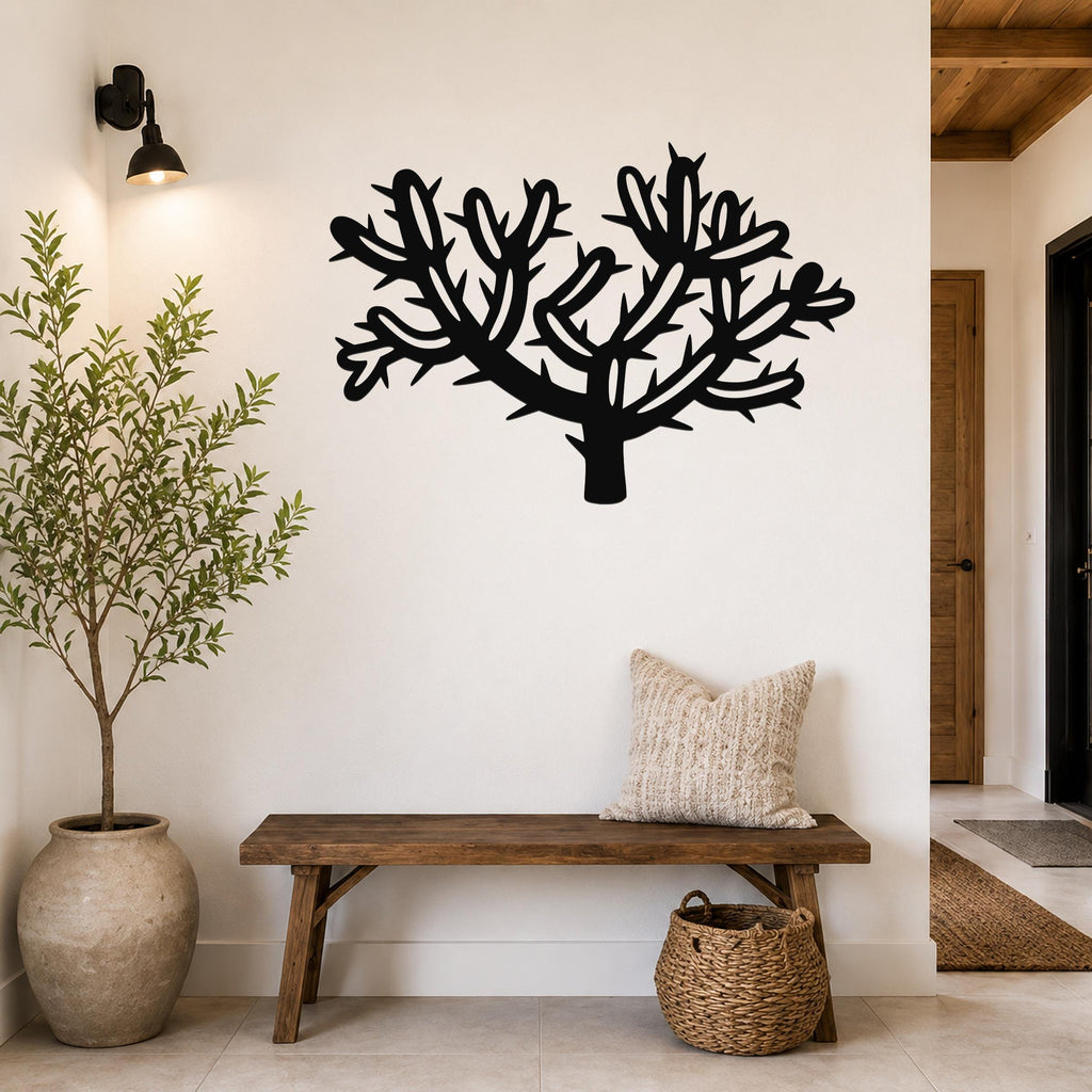 Black metal cholla cactus wall art with branching cutouts, mounted on a white wall above a wooden bench in a entryway.