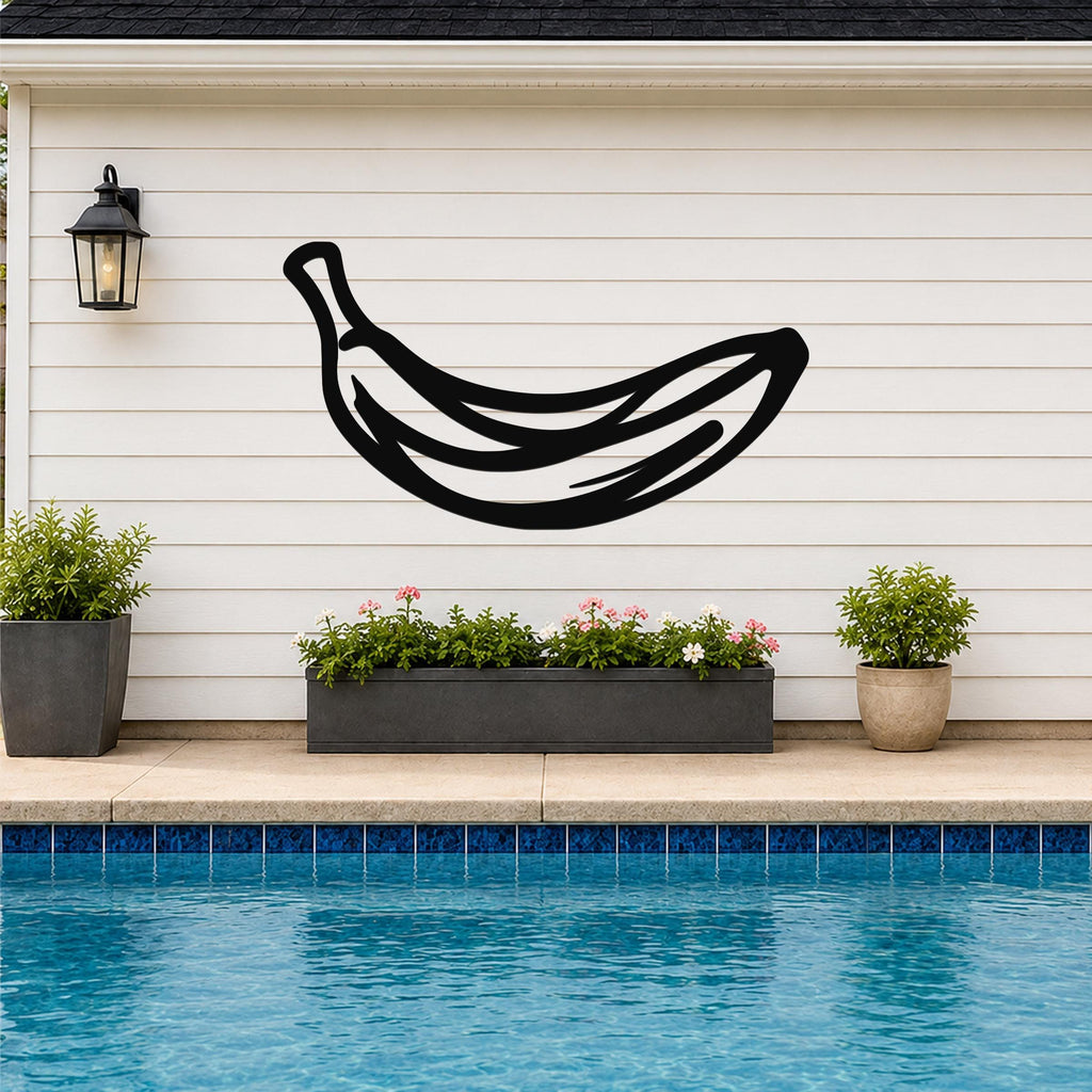 Black metal banana wall art with internal line cutouts, mounted on a white horizontal siding wall above a poolside planter.