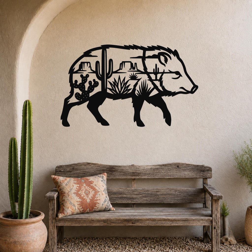 Black metal wall art in the silhouette of a javelina, with desert landscape cutouts including cacti and mountains, mounted on a beige wall above a wooden bench in a rustic living space.
