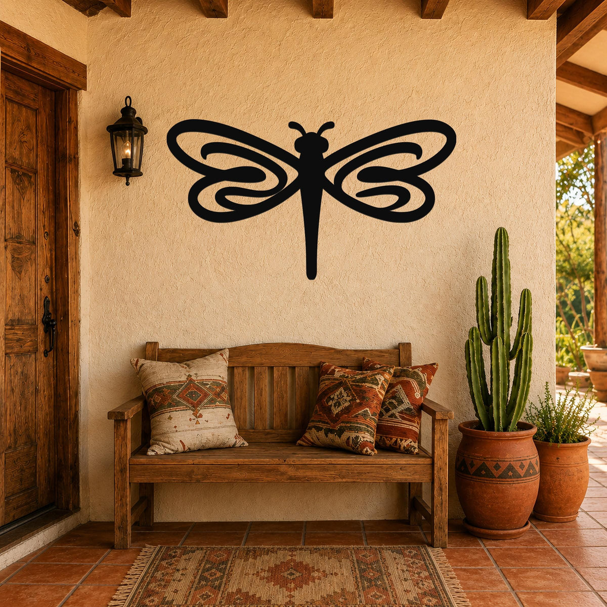 Black metal dragonfly wall art with flowing wing cutouts, mounted on a stucco wall above a wooden bench in a patio entryway.