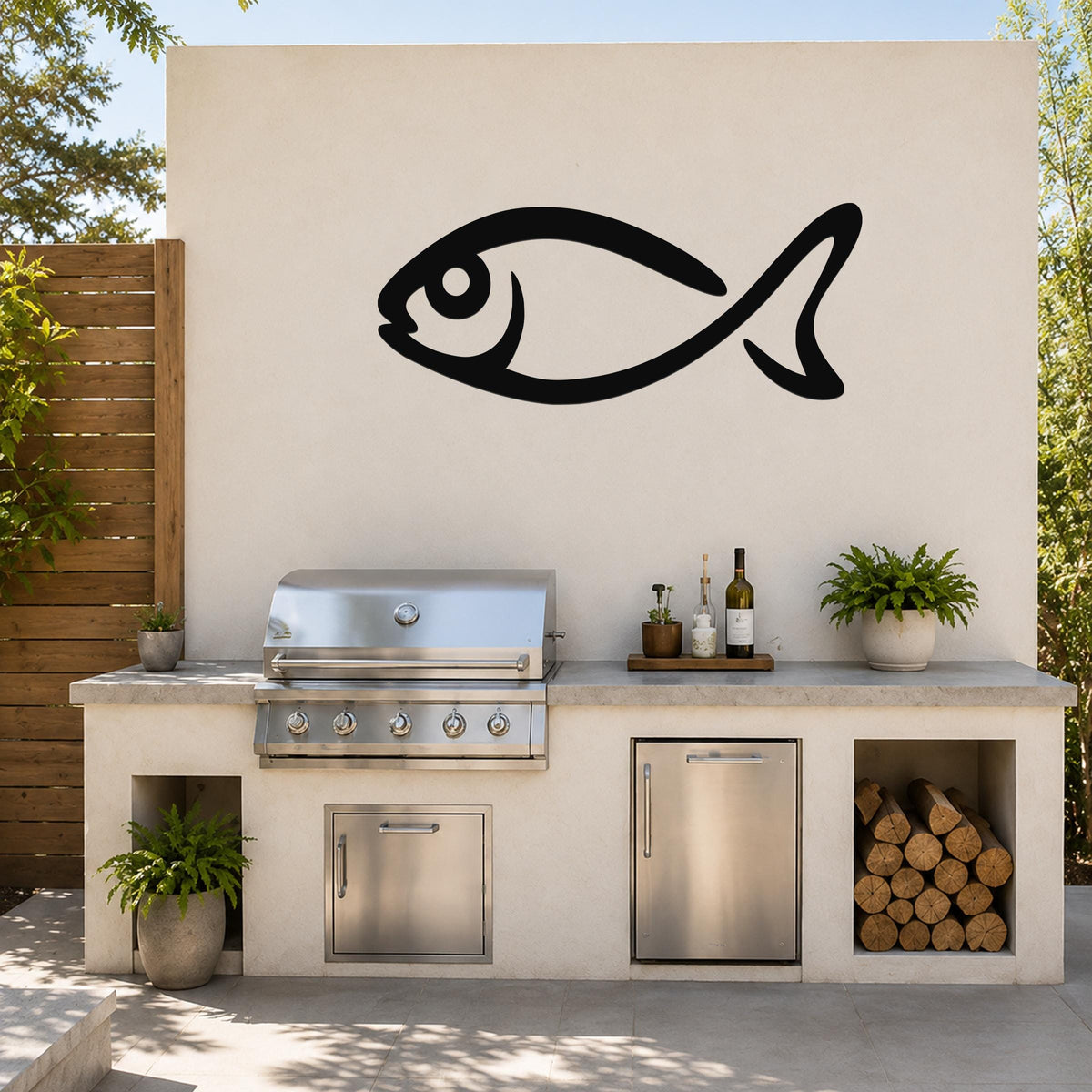 Black metal fish silhouette wall art mounted on a light-colored outdoor wall above a kitchen counter with a grill and storage.