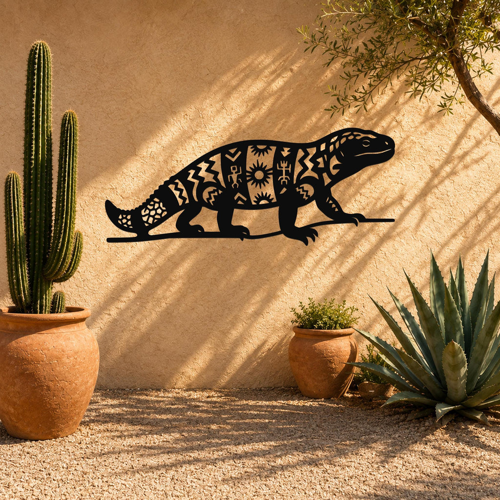 Black metal wall art of a Gila monster with intricate geometric and sun motif cutouts, mounted on a stucco outdoor wall above potted cacti and succulents.