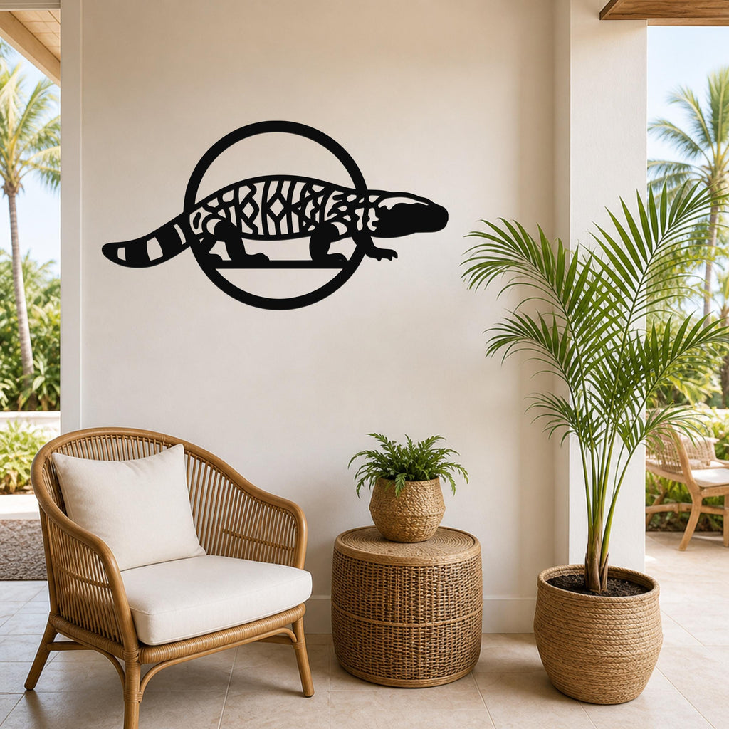 Black metal Gila monster wall art with intricate internal cutouts, mounted on a light-colored wall above a wicker chair in a tropical patio setting.