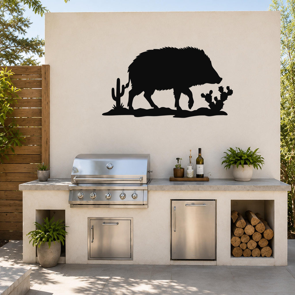 Black metal javelina wall art with cactus cutouts, mounted on an outdoor kitchen wall above a stainless steel grill.