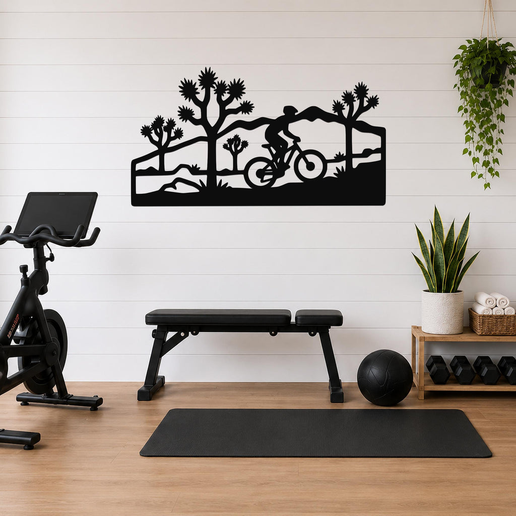 Black metal wall art with a silhouette of a cyclist and Joshua trees, mounted on a white shiplap wall above a workout bench in a home gym.