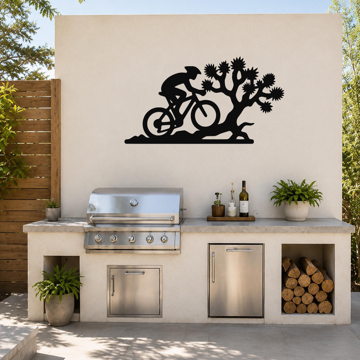 Black metal wall art featuring a cyclist silhouette and Joshua tree cutout, mounted on an outdoor patio wall above a kitchen counter.