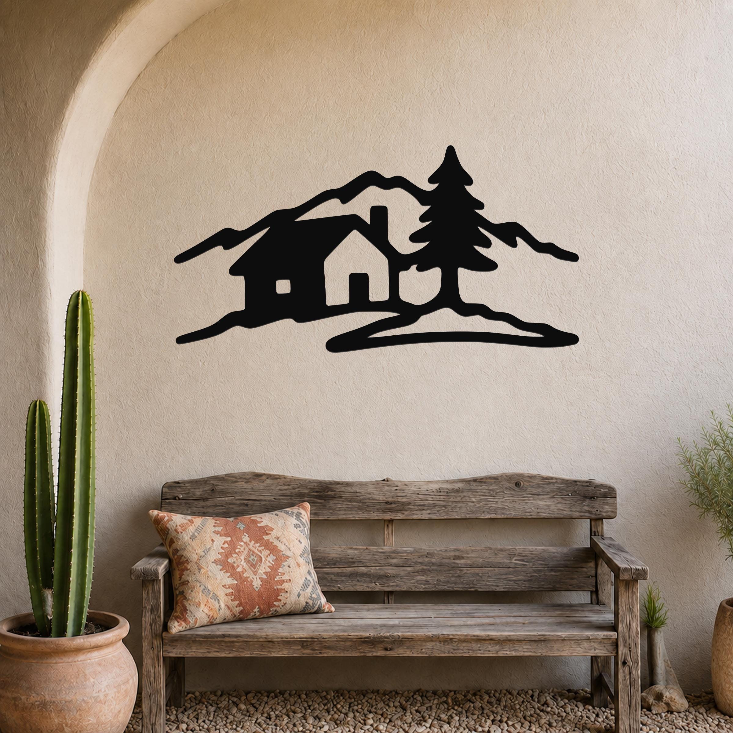 Black metal wall art silhouette of a cabin, pine tree, and mountains, mounted on a textured wall above a wooden bench in a rustic entryway.