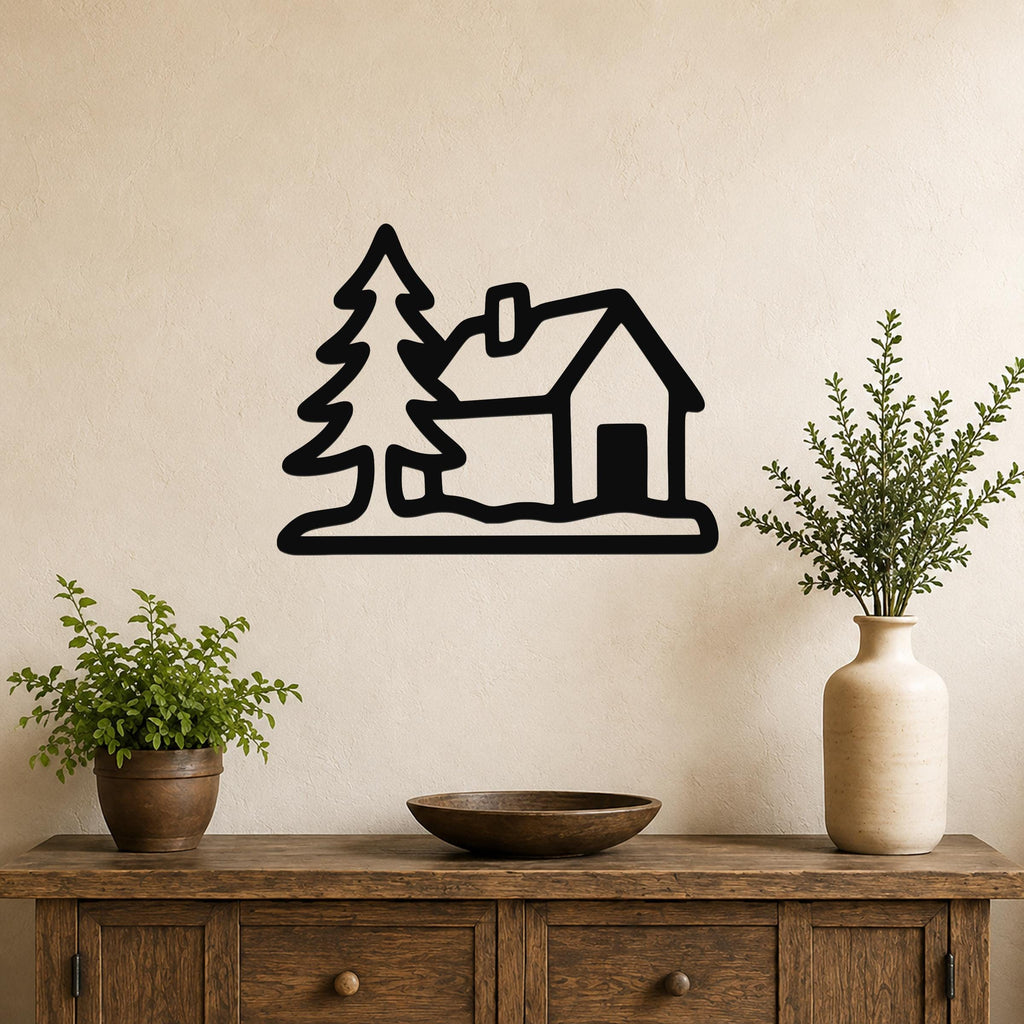 Black metal wall art silhouette of a cabin and pine trees, mounted on a beige wall above a wooden console table with potted plants.